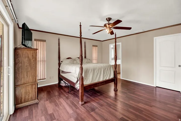 Bedroom with dark wood-style floors, ceiling fan, ornamental molding, and ensuite bath