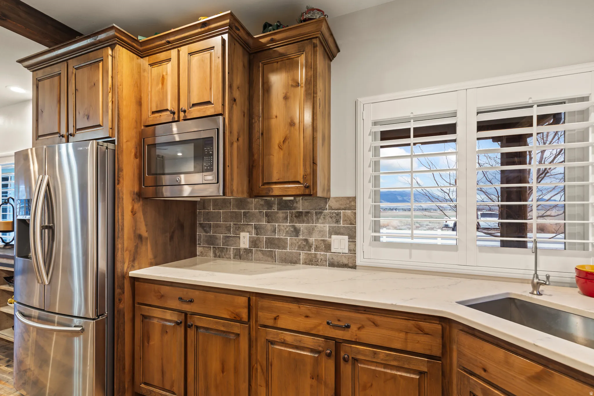 Kitchen featuring stainless steel appliances, light stone counters, wood finish cabinetry, and backsplash