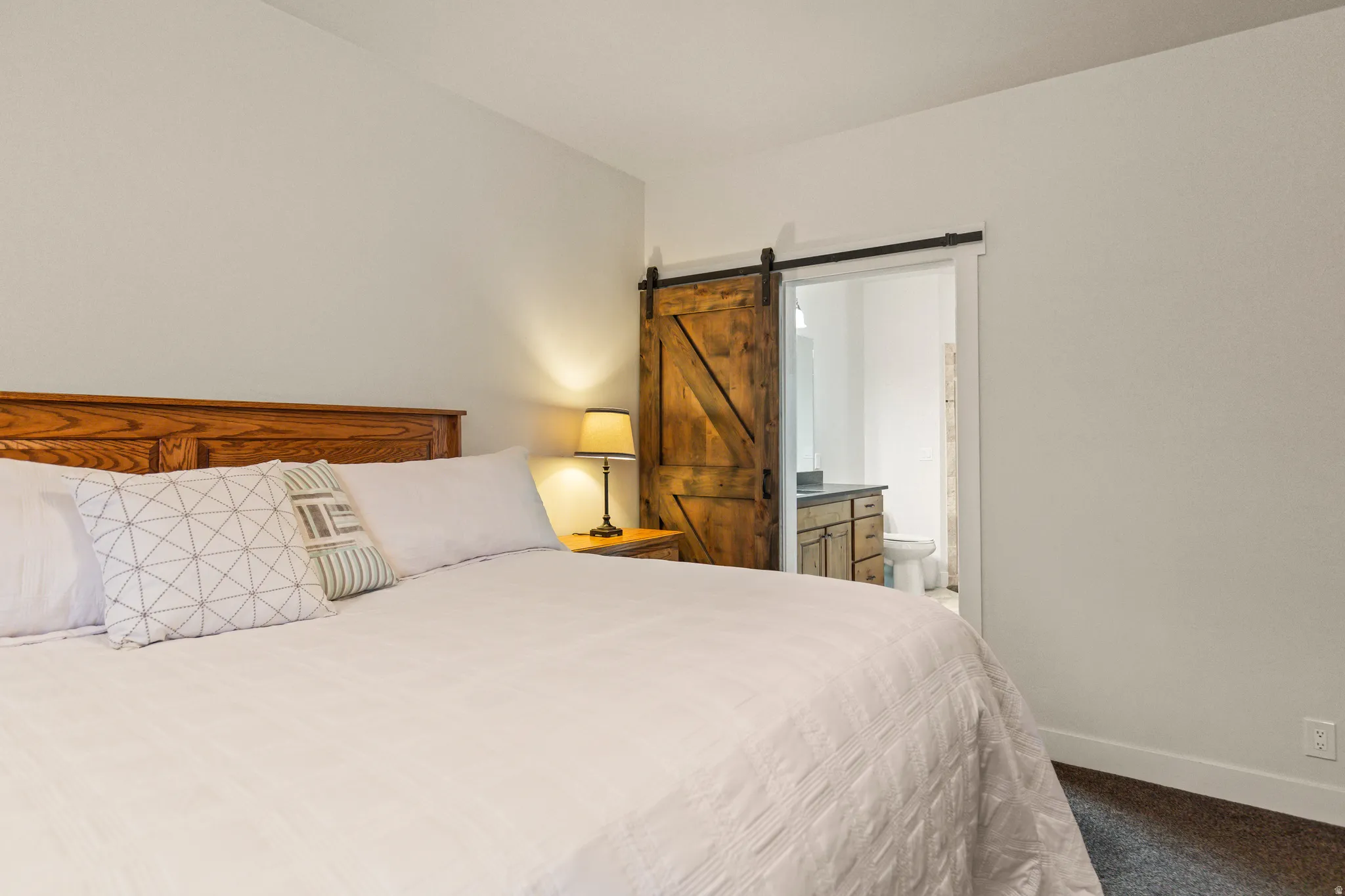 Bedroom with a barn door, dark carpet, and ensuite bathroom