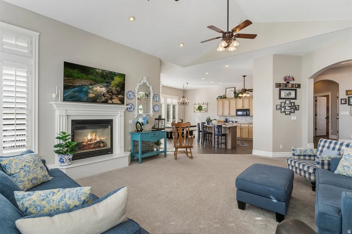 Carpeted living room featuring a ceiling fan, a glass covered fireplace, recessed lighting, lofted ceiling, and arched walkways