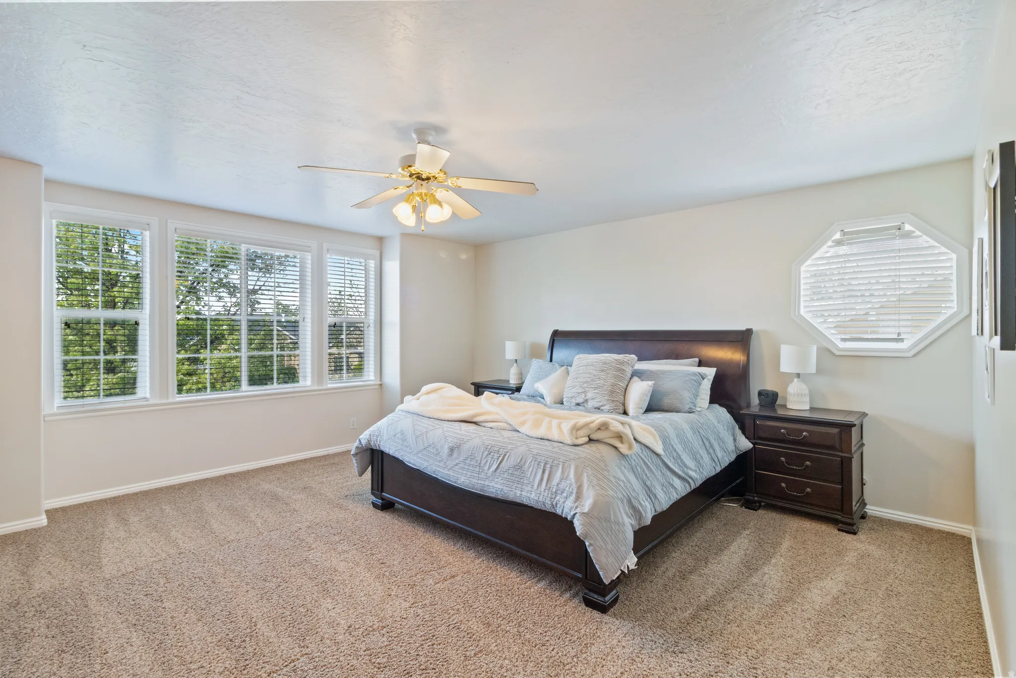 Primary bedroom with light colored carpet, ceiling fan, and a textured ceiling