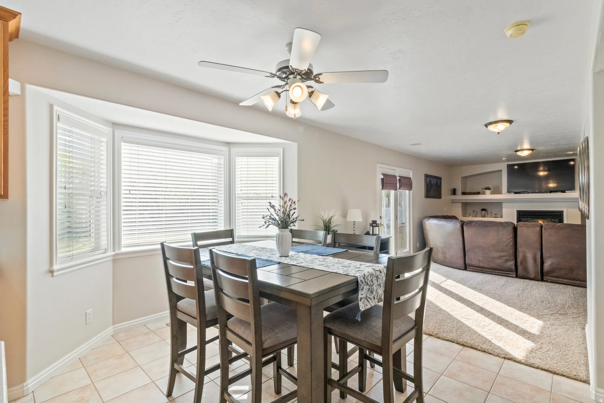 Dining space featuring light tile patterned flooring, a ceiling fan, fireplace, and light carpet