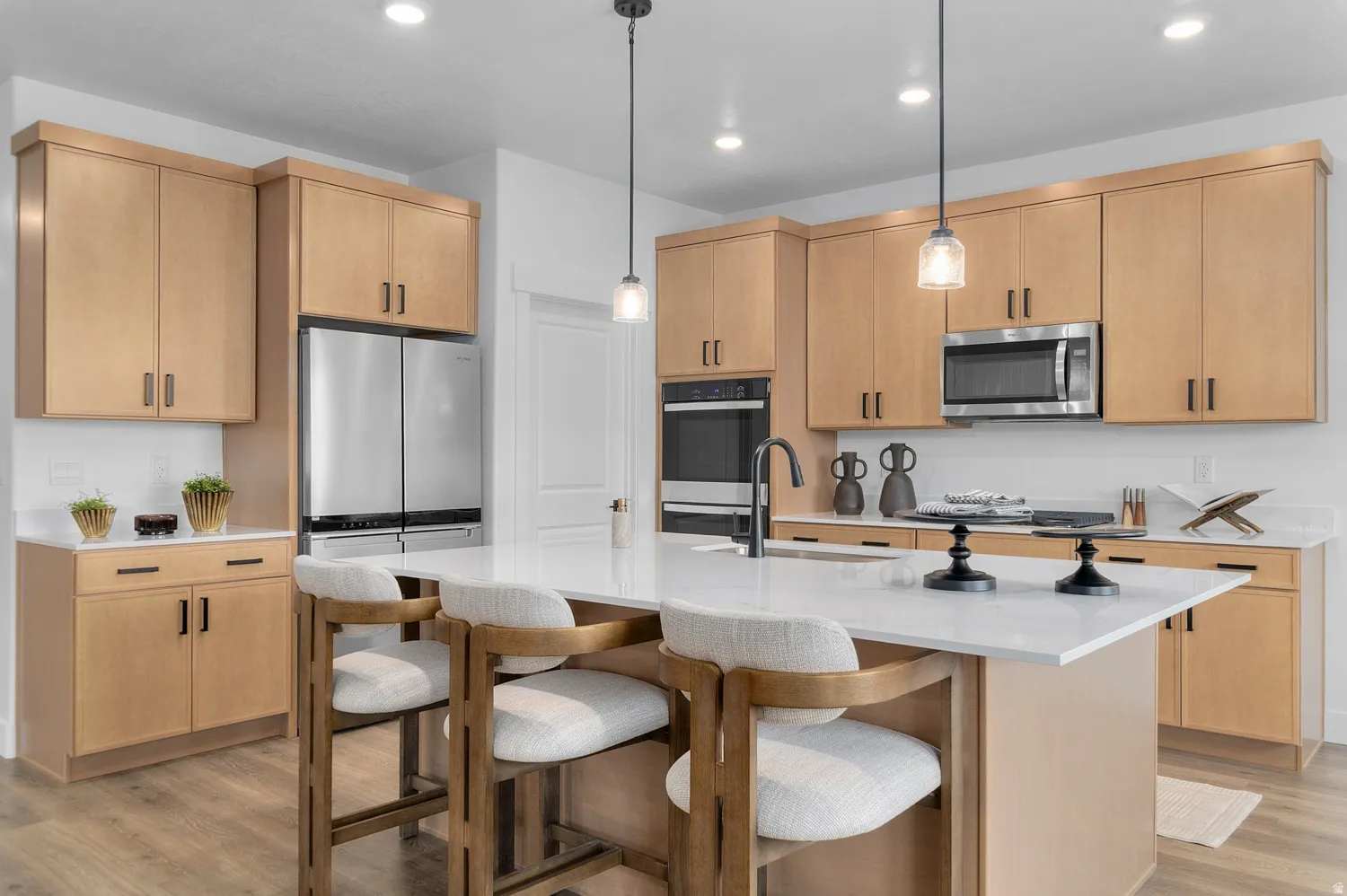 Kitchen featuring light stone countertops, an island with sink, light wood finish cabinetry, light wood-type flooring, and a kitchen breakfast bar