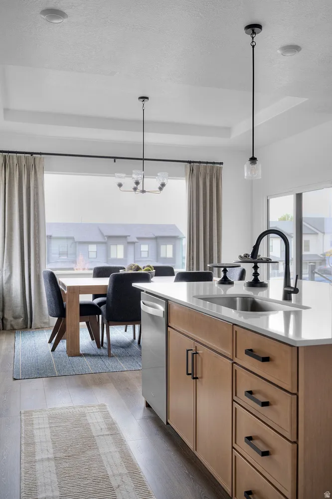 Kitchen with a center island with sink, light wood finished floors, a raised ceiling, a textured ceiling, and a chandelier