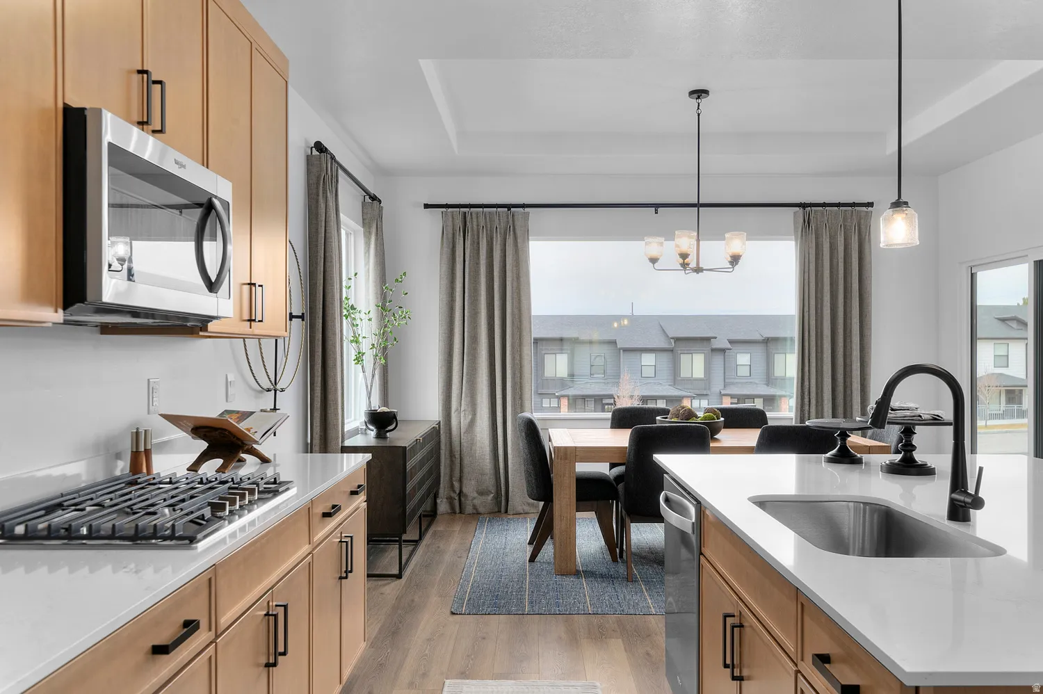 Kitchen featuring a raised ceiling, light wood-style flooring, stainless steel appliances, light stone counters, and hanging lights