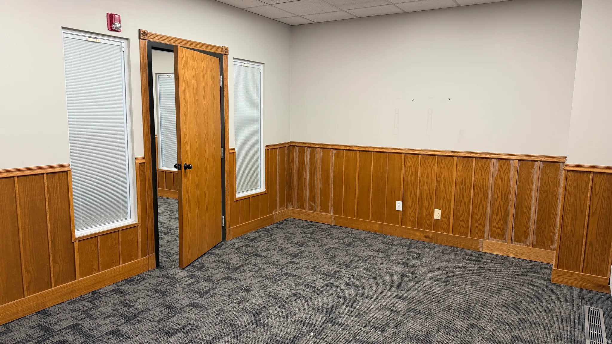 Room featuring wood-finish wainscoting, neutral wall paint, and patterned carpet flooring