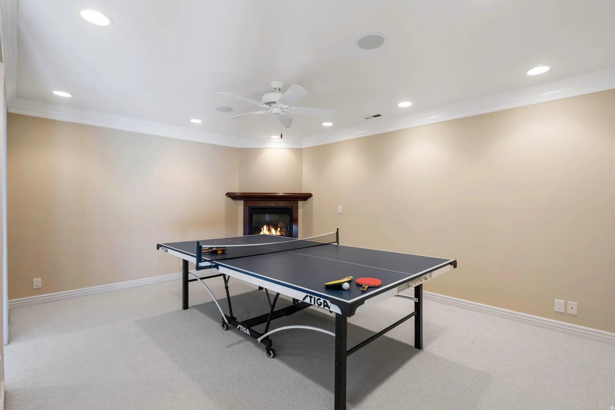 Playroom featuring a glass covered fireplace, light carpet, recessed lighting, a ceiling fan, and ornamental molding