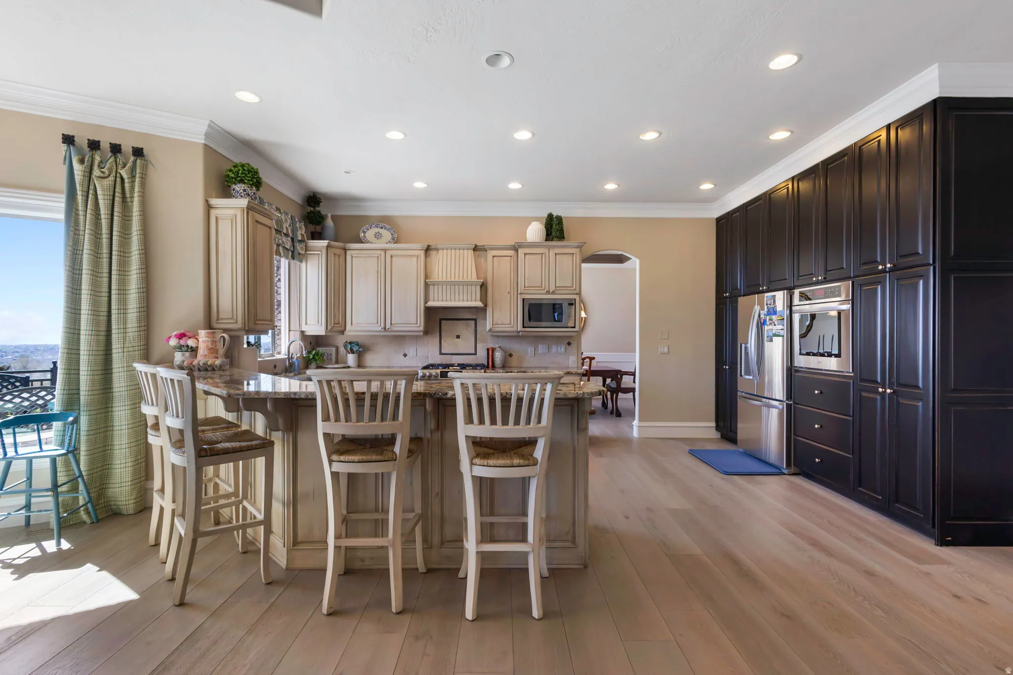 Kitchen featuring a peninsula, arched walkways, a breakfast bar area, light stone countertops, and stainless steel appliances