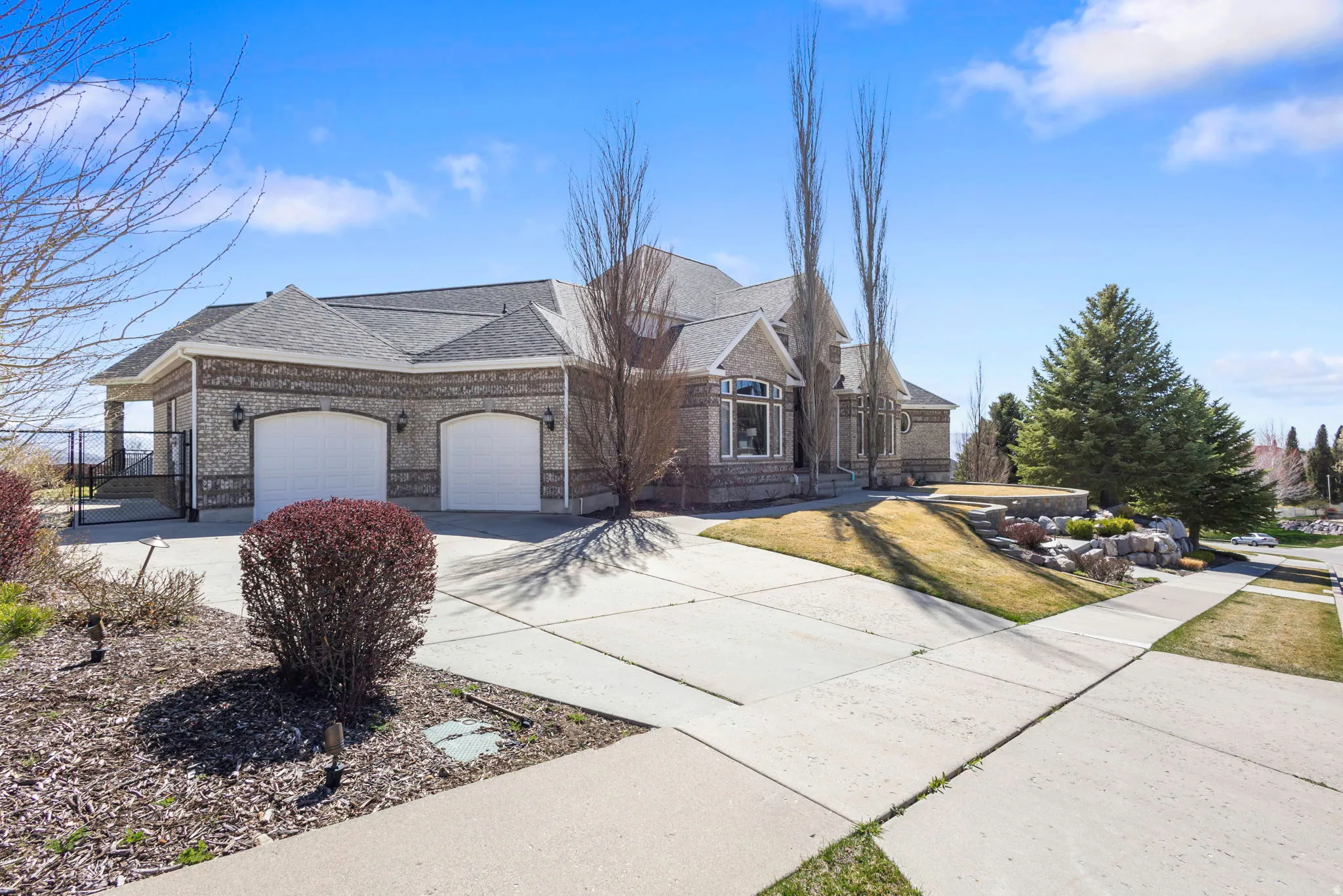 View of front of house with concrete driveway, a garage, a shingled roof, brick siding, and a gate