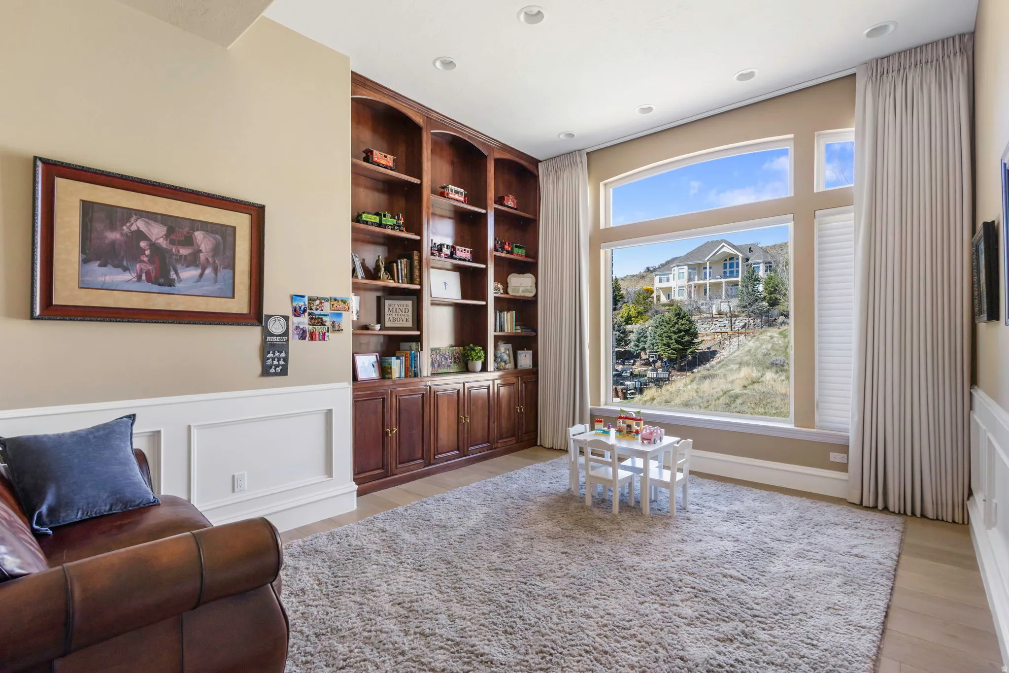 Living area with built in shelves, wainscoting, a decorative wall, and light wood finished floors