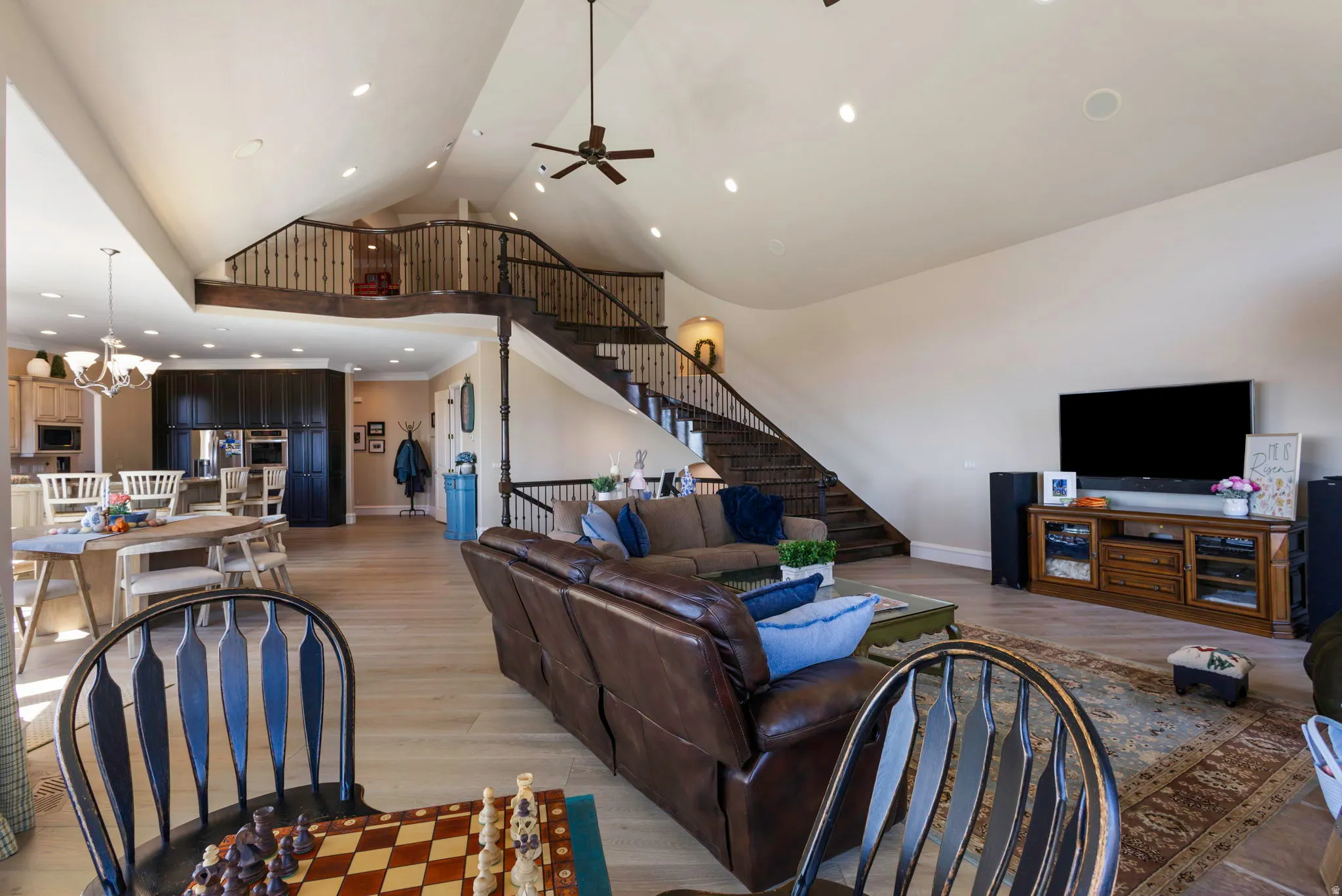 Living room with a high ceiling, light wood-style flooring, a ceiling fan, and suspended lighting