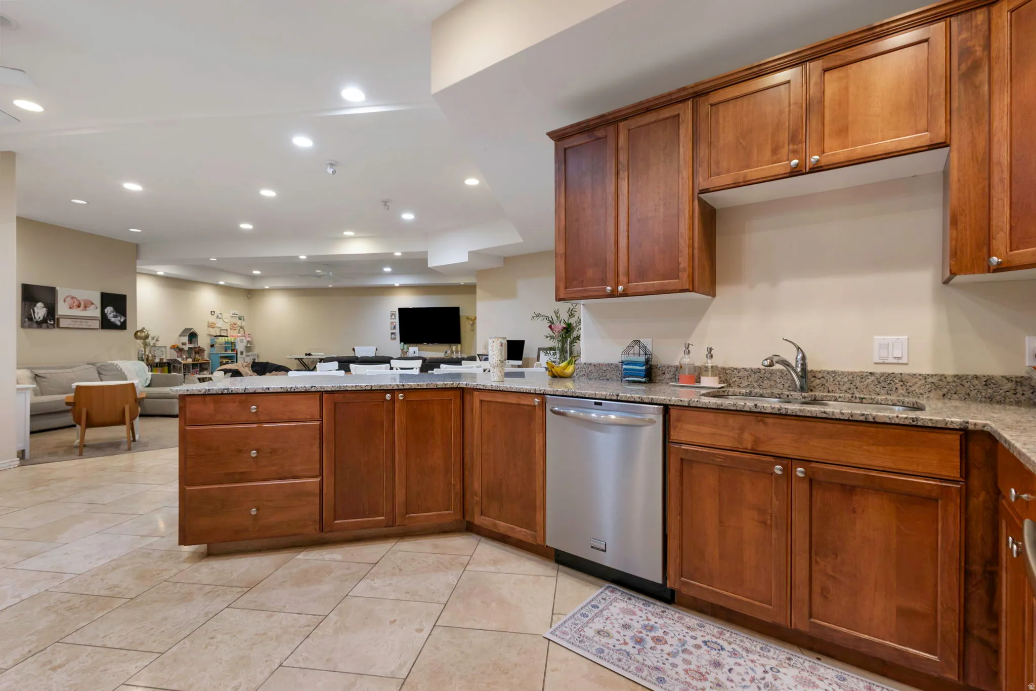 Kitchen featuring a peninsula, open floor plan, light stone countertops, stainless steel dishwasher, and wood finish cabinets