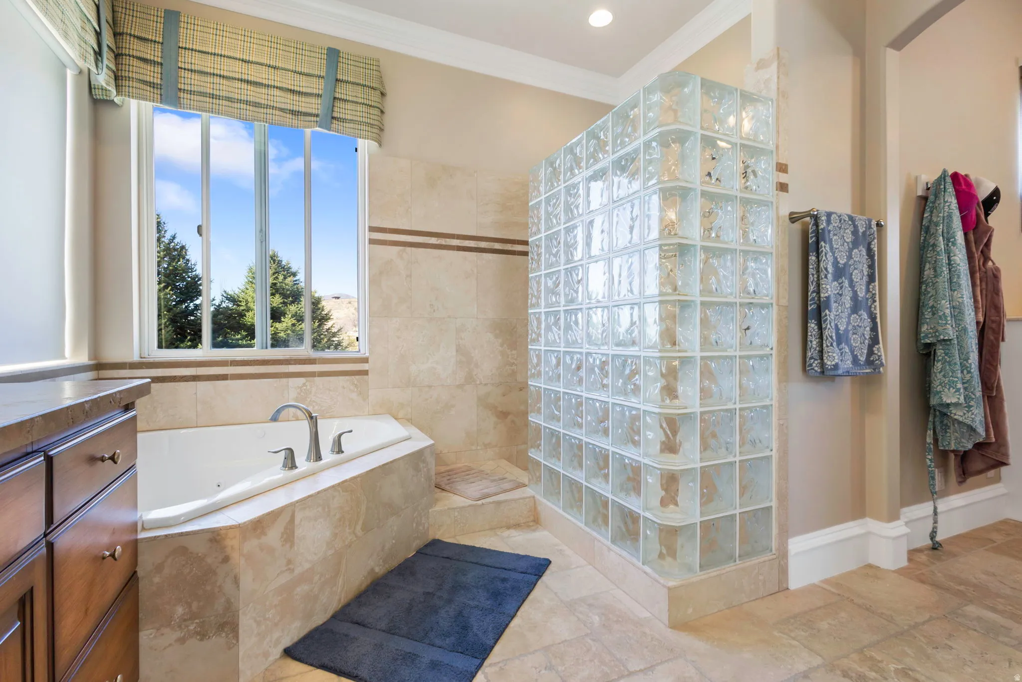 Bathroom featuring a walk in shower, crown molding, a bath, vanity, and stone tile floors