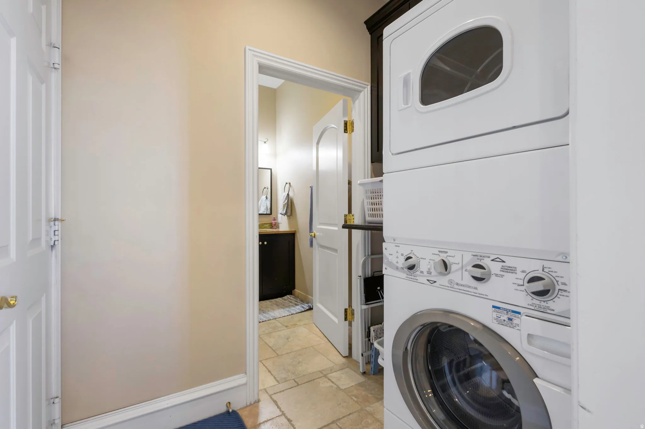 Laundry room with stone tile flooring and stacked washer and dryer