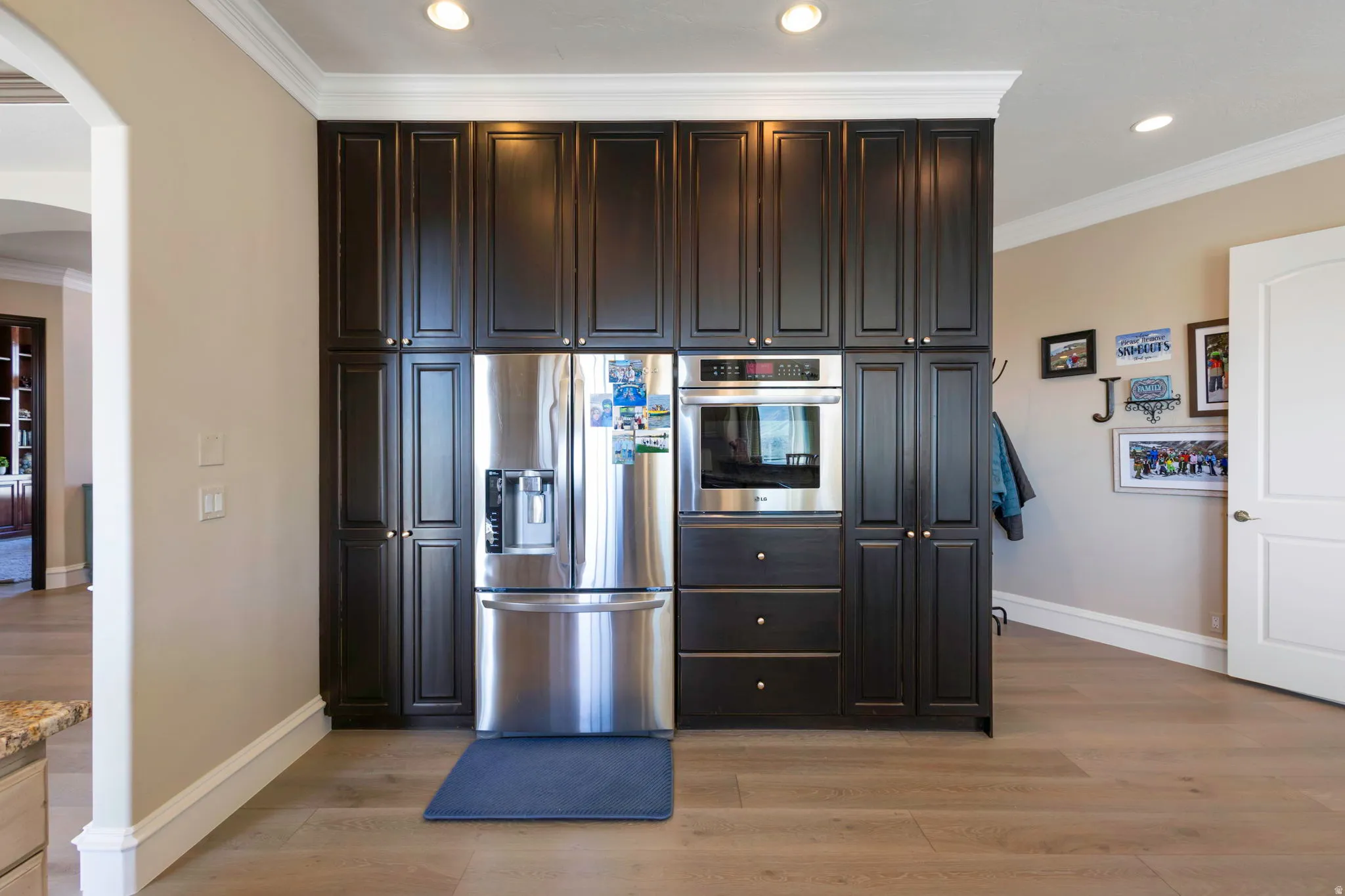 Kitchen featuring crown molding, stainless steel appliances, dark wood finish cabinets, light wood-style floors, and arched walkways