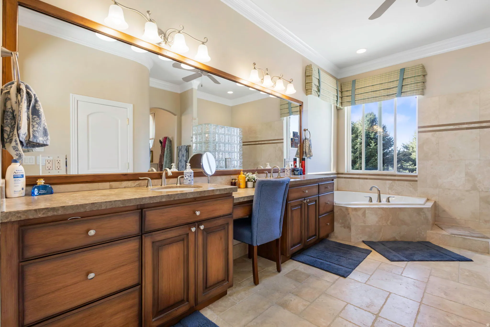 Full bath featuring a ceiling fan, vanity, stone tile flooring, a garden tub, and ornamental molding