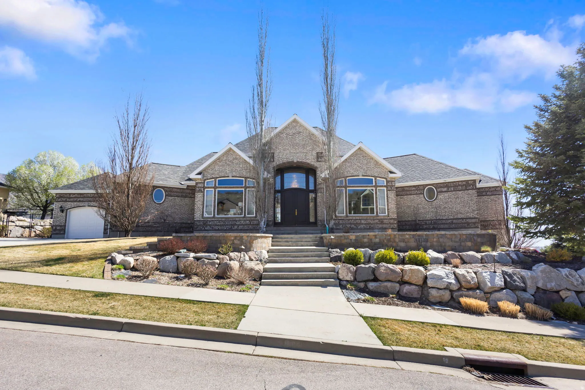 French country inspired facade featuring an attached garage, a shingled roof, brick siding, and driveway