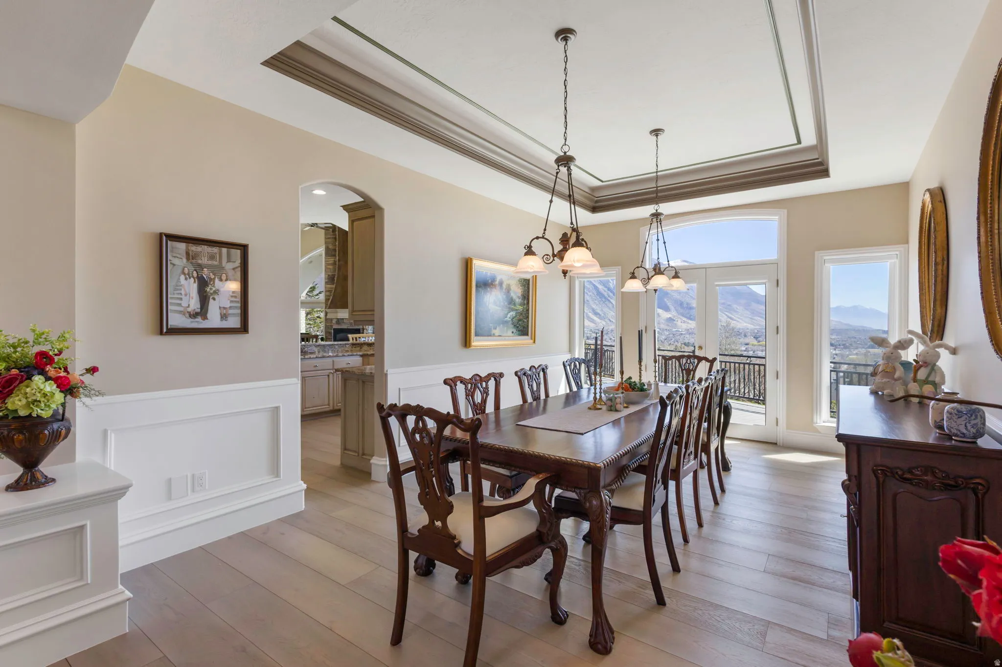 Dining space with a raised ceiling, a mountain view, suspended lighting, arched walkways, and light wood-type flooring