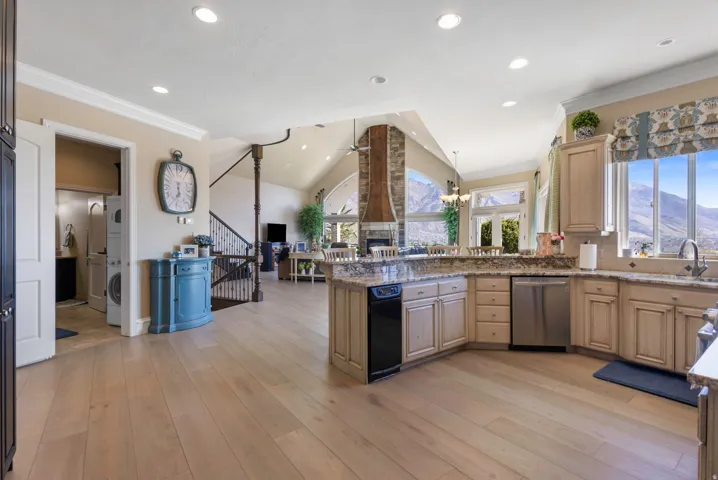 Kitchen featuring a peninsula, ceiling fan, vaulted ceiling, ornamental molding, and light stone countertops
