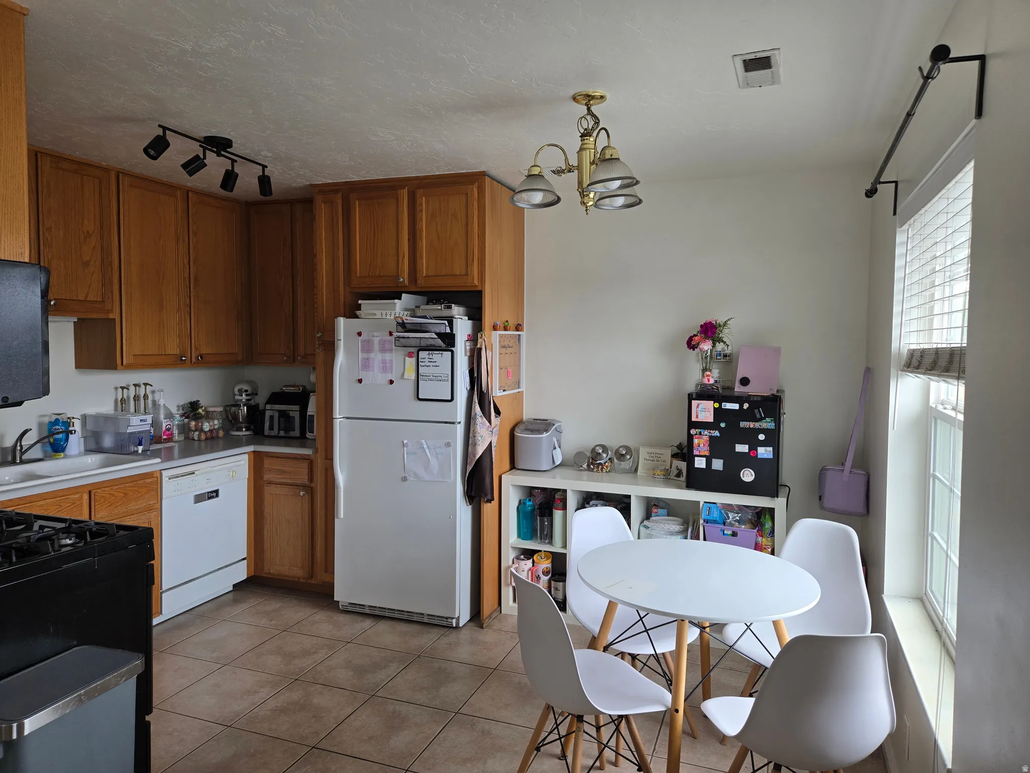 Kitchen with wood finish cabinetry, white appliances, a chandelier, a textured ceiling, and light tile patterned flooring