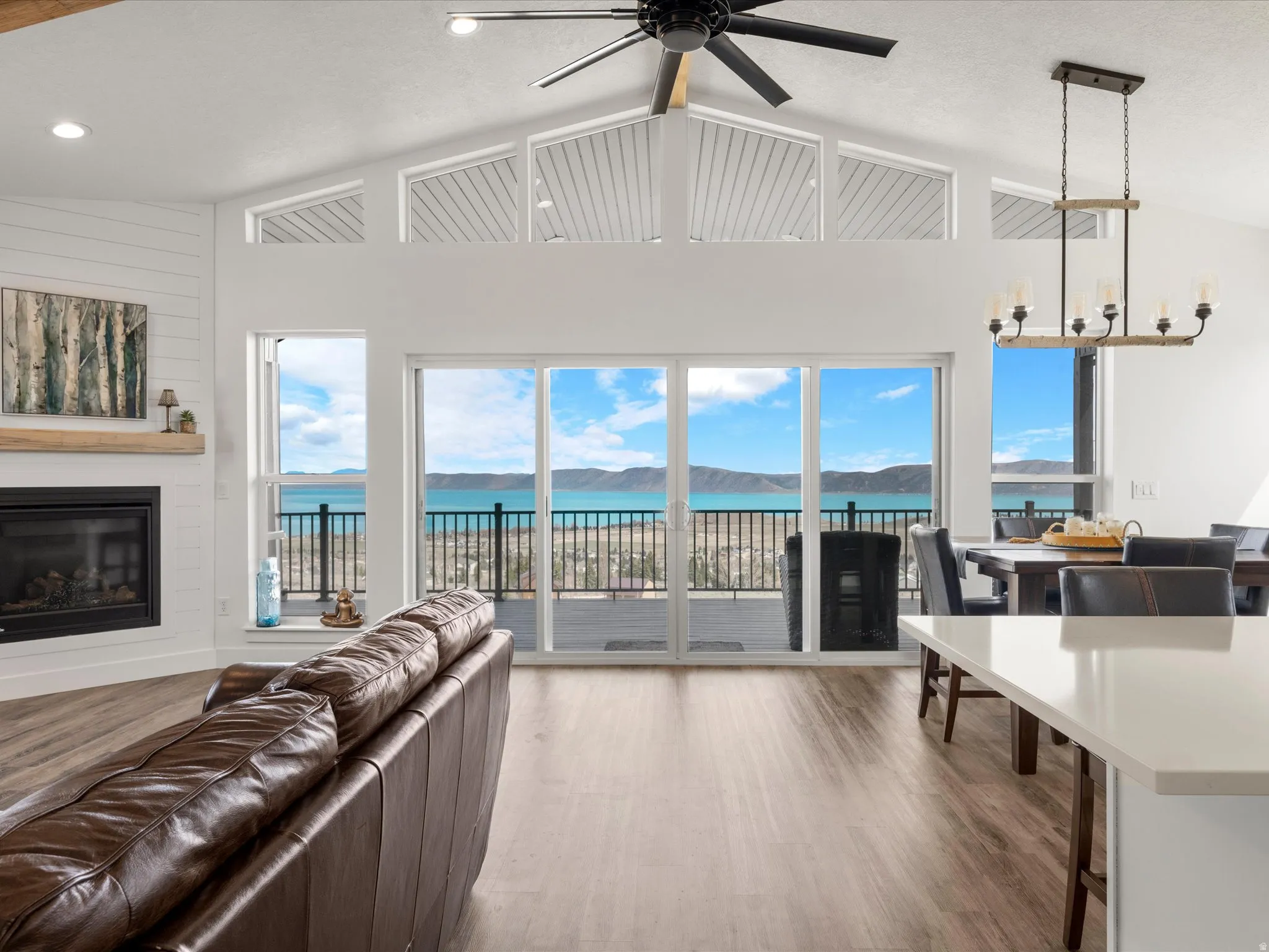 Living room with Luxury vinyl floors, a chandelier, a ceiling fan, a glass covered fireplace, and a high ceiling