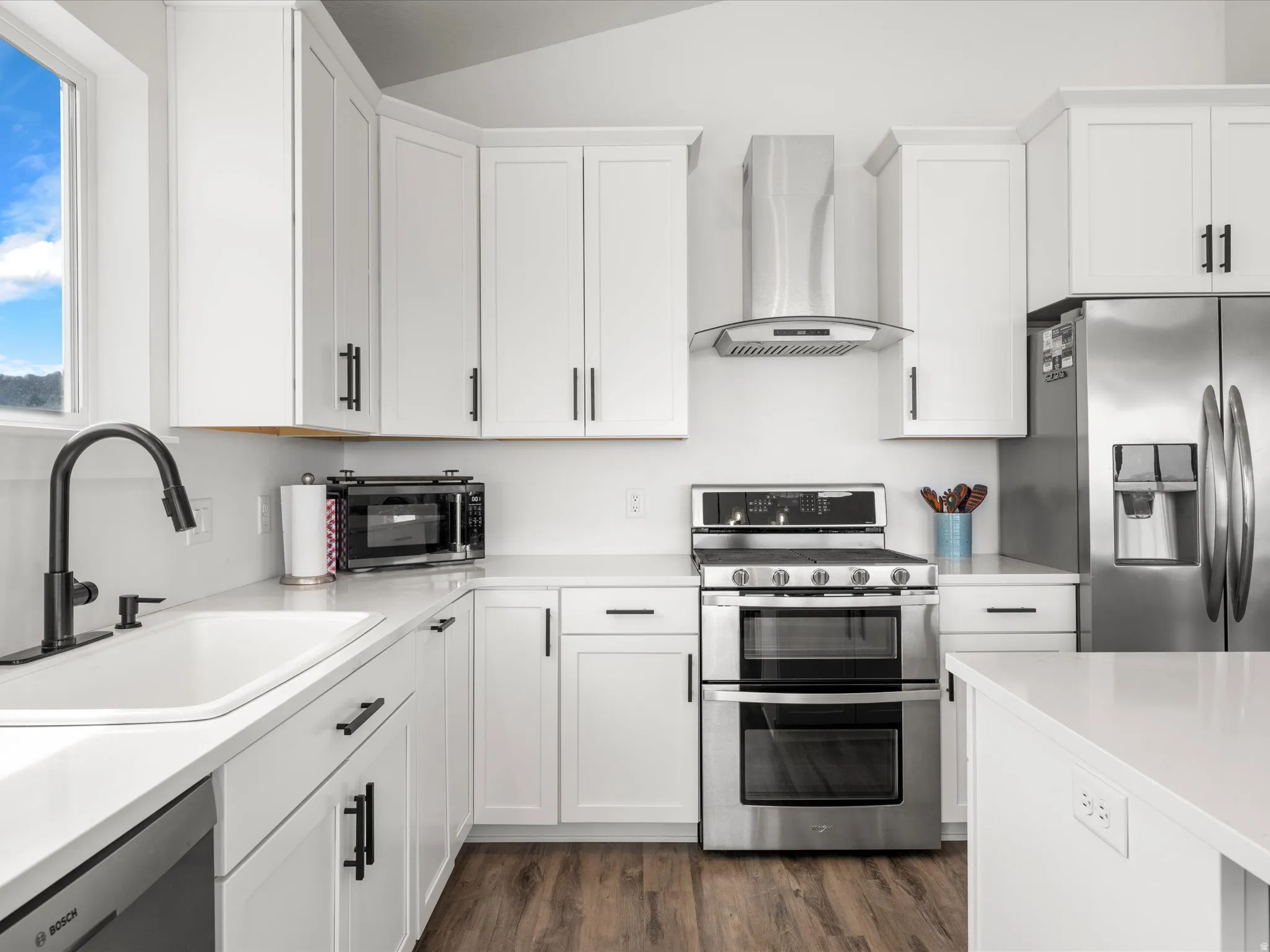 Kitchen with stainless steel appliances, white cabinets, dark wood finished floors, and lofted ceiling