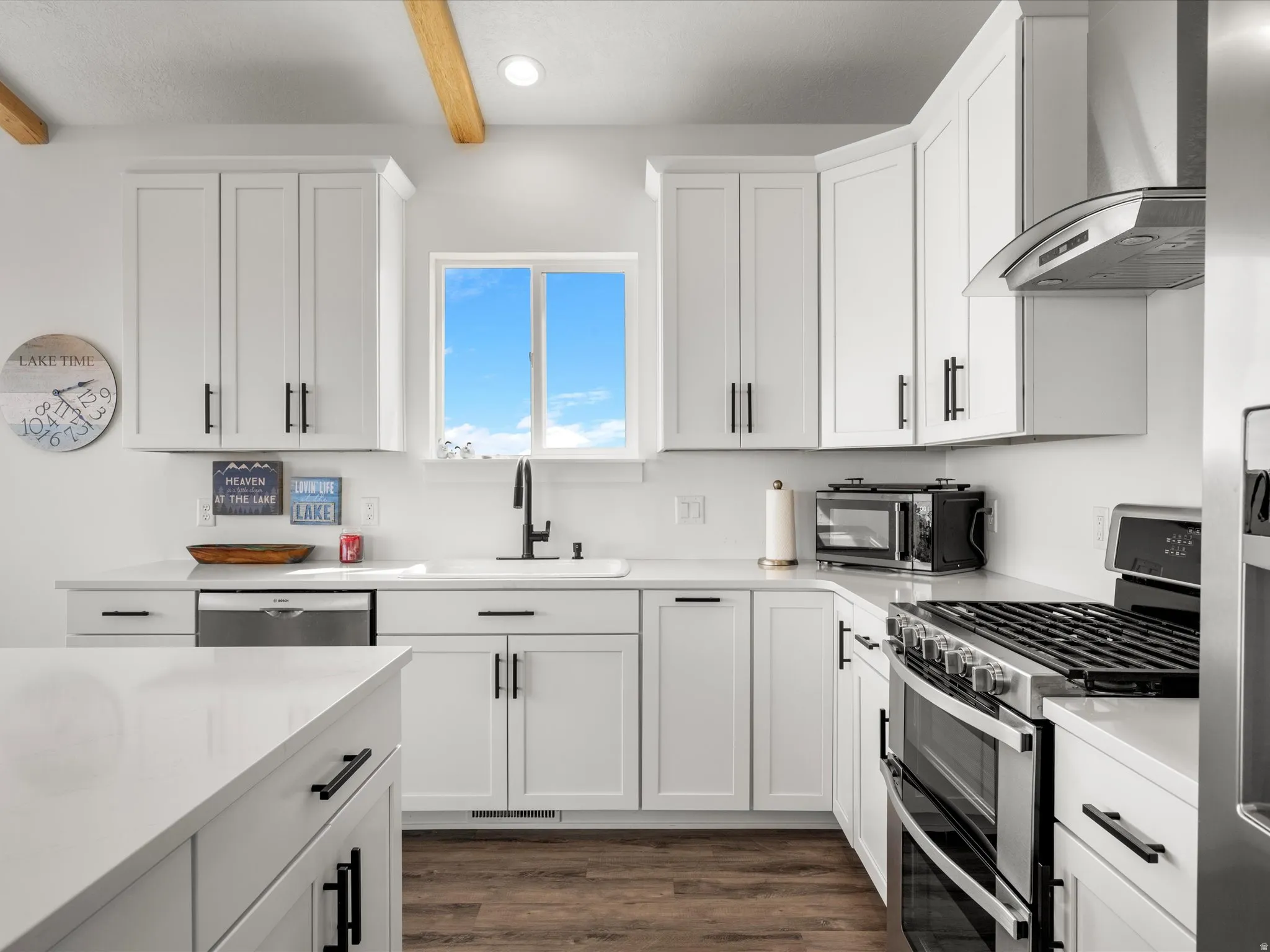 Kitchen featuring stainless steel appliances, white cabinets, dark wood-style flooring, beam ceiling, and light stone countertops