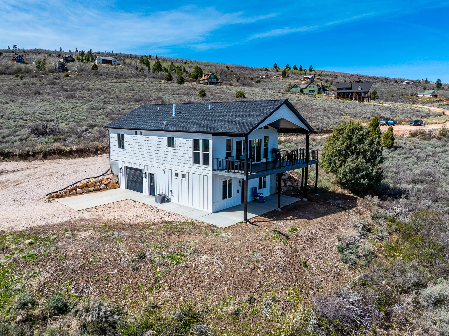 Rear view of house featuring a patio, a garage, a shingled roof, concrete driveway, and a rural view
