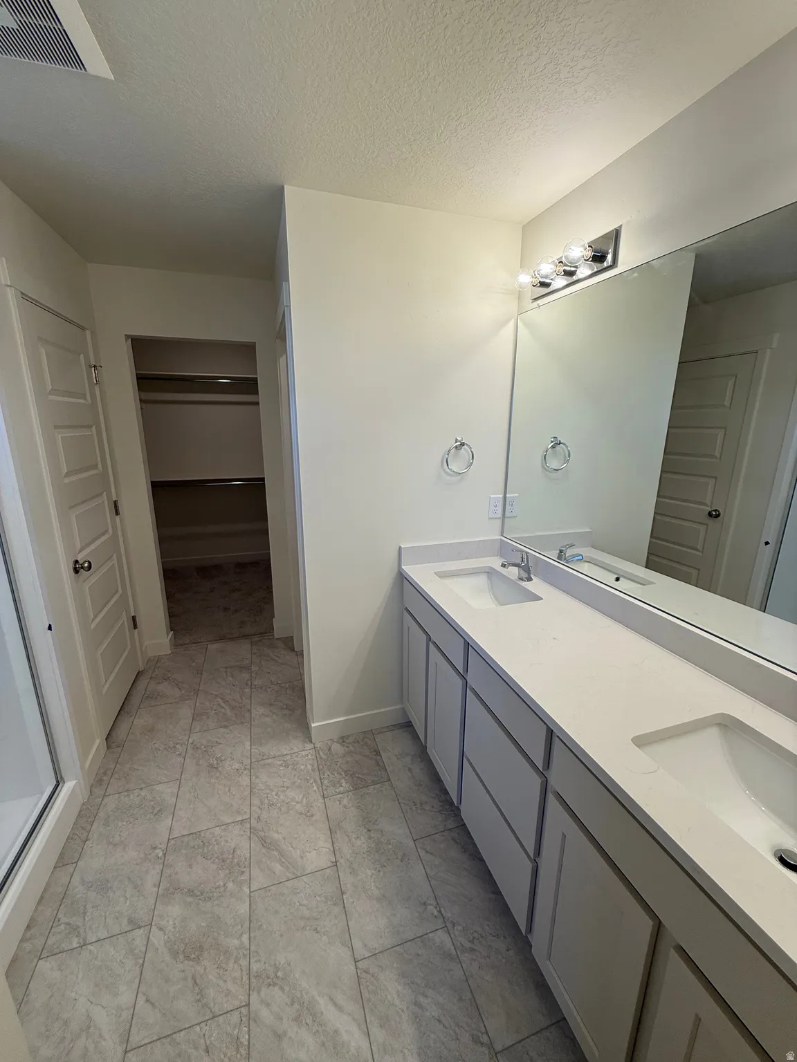 Dual vanity with integrated sinks, expansive counter space, light-toned cabinetry, large wall-mounted mirror, and tile flooring