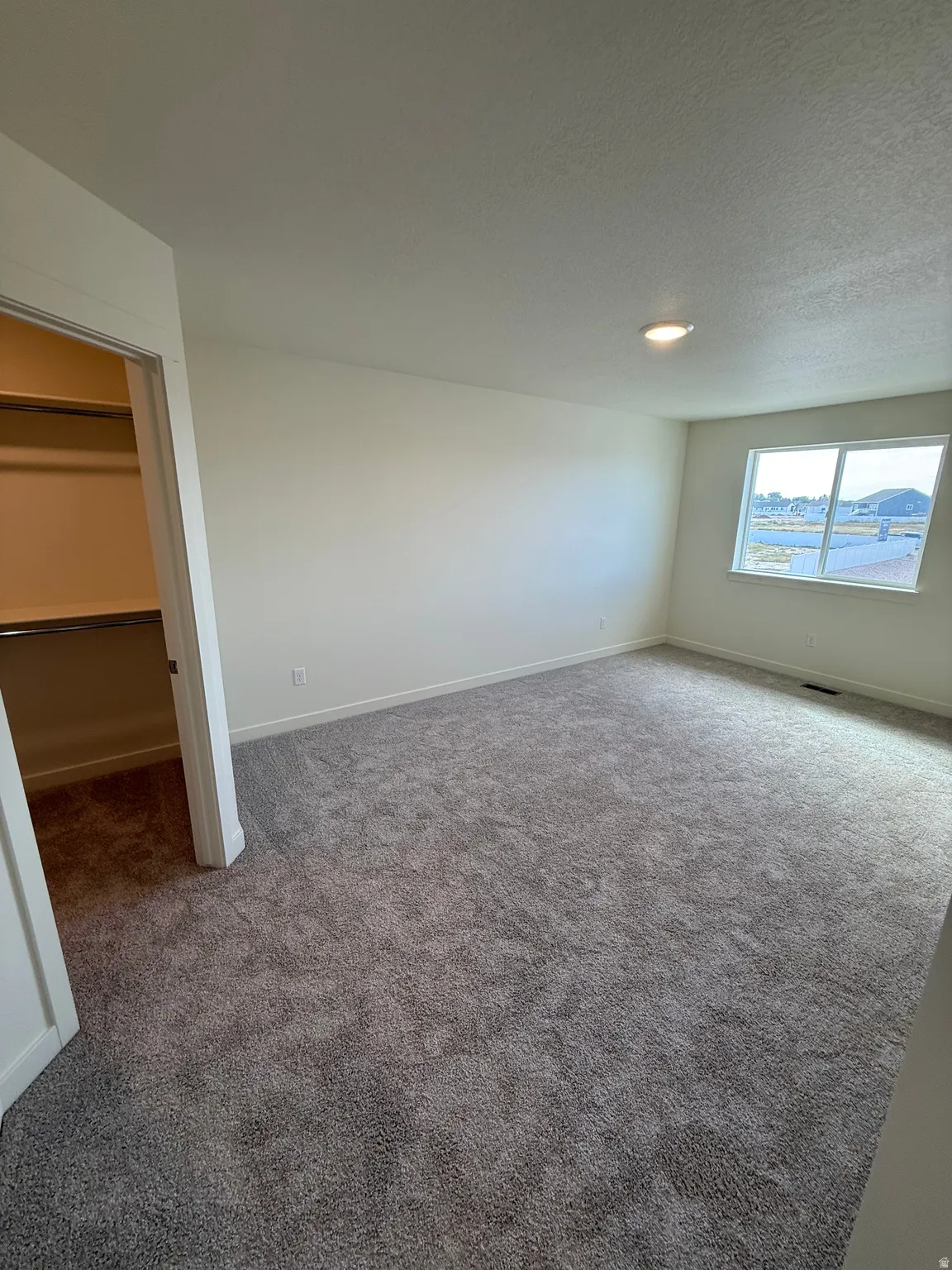 Spacious room with plush gray carpeting, neutral wall paint, and a large window