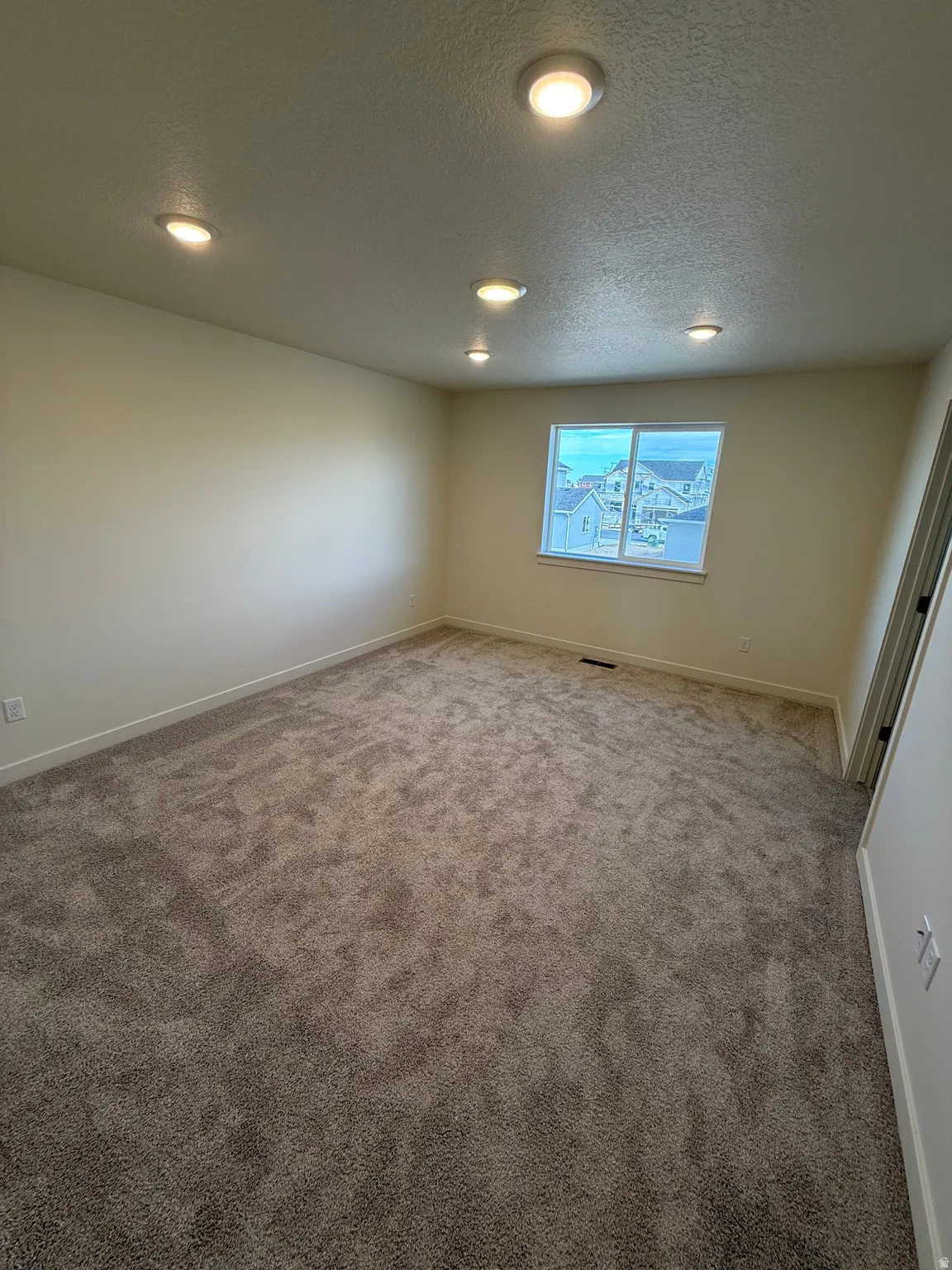 Wall-to-wall carpeting, recessed ceiling lighting, and a single window with white trim