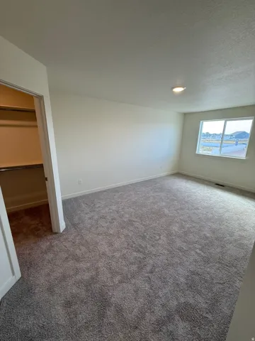 Spacious room with plush gray carpeting, neutral wall paint, and a large window