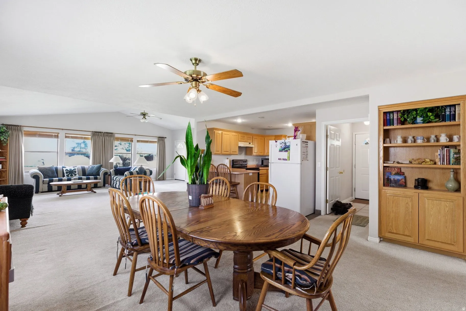 Dining area featuring light colored carpet, ceiling fan, and vaulted ceiling