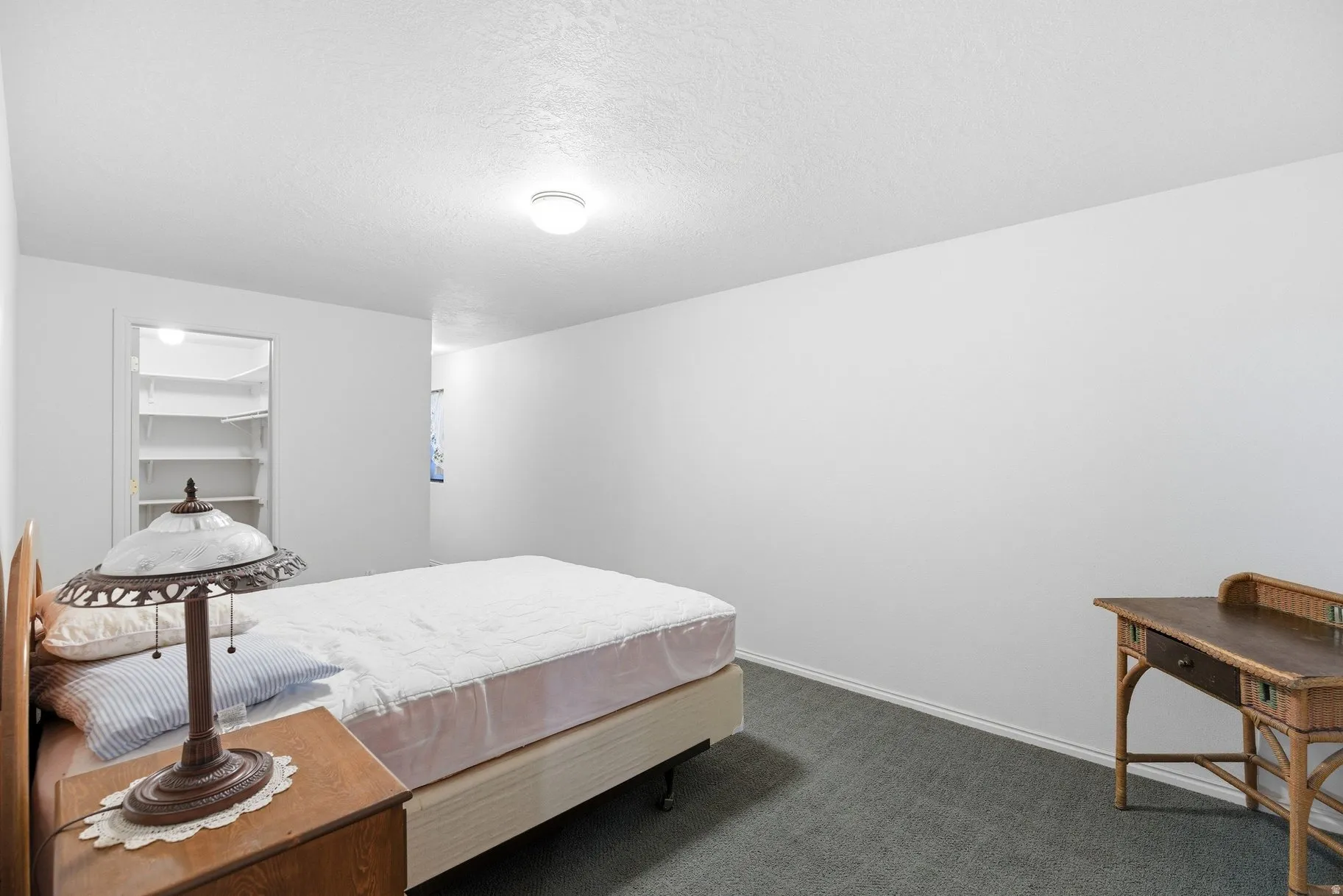 Bedroom with dark colored carpet, a textured ceiling, and a walk in closet