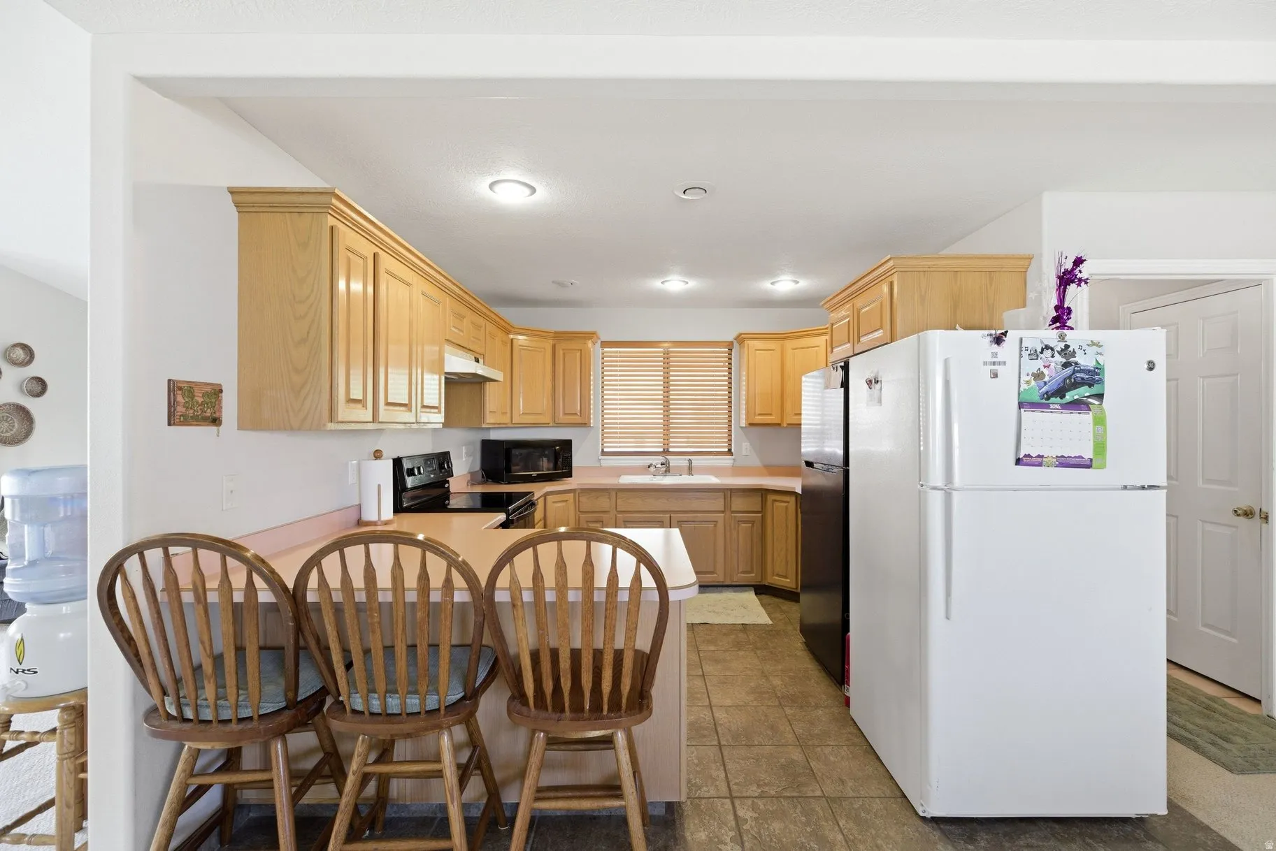 Kitchen featuring light wood finish cabinetry, black appliances, light countertops, a peninsula, and recessed lighting