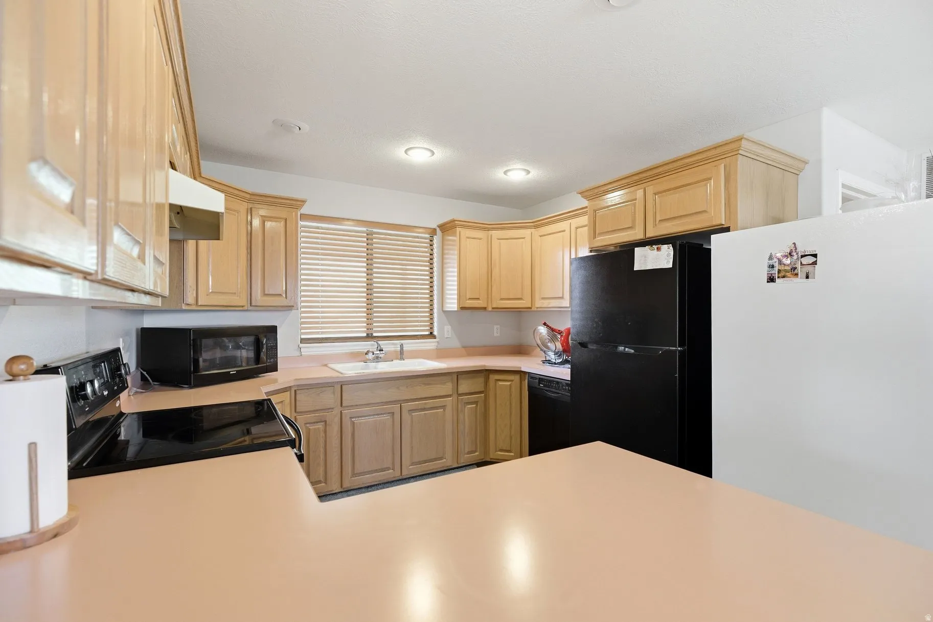 Kitchen featuring black appliances, light wood finish cabinets, light countertops, range hood, and a peninsula