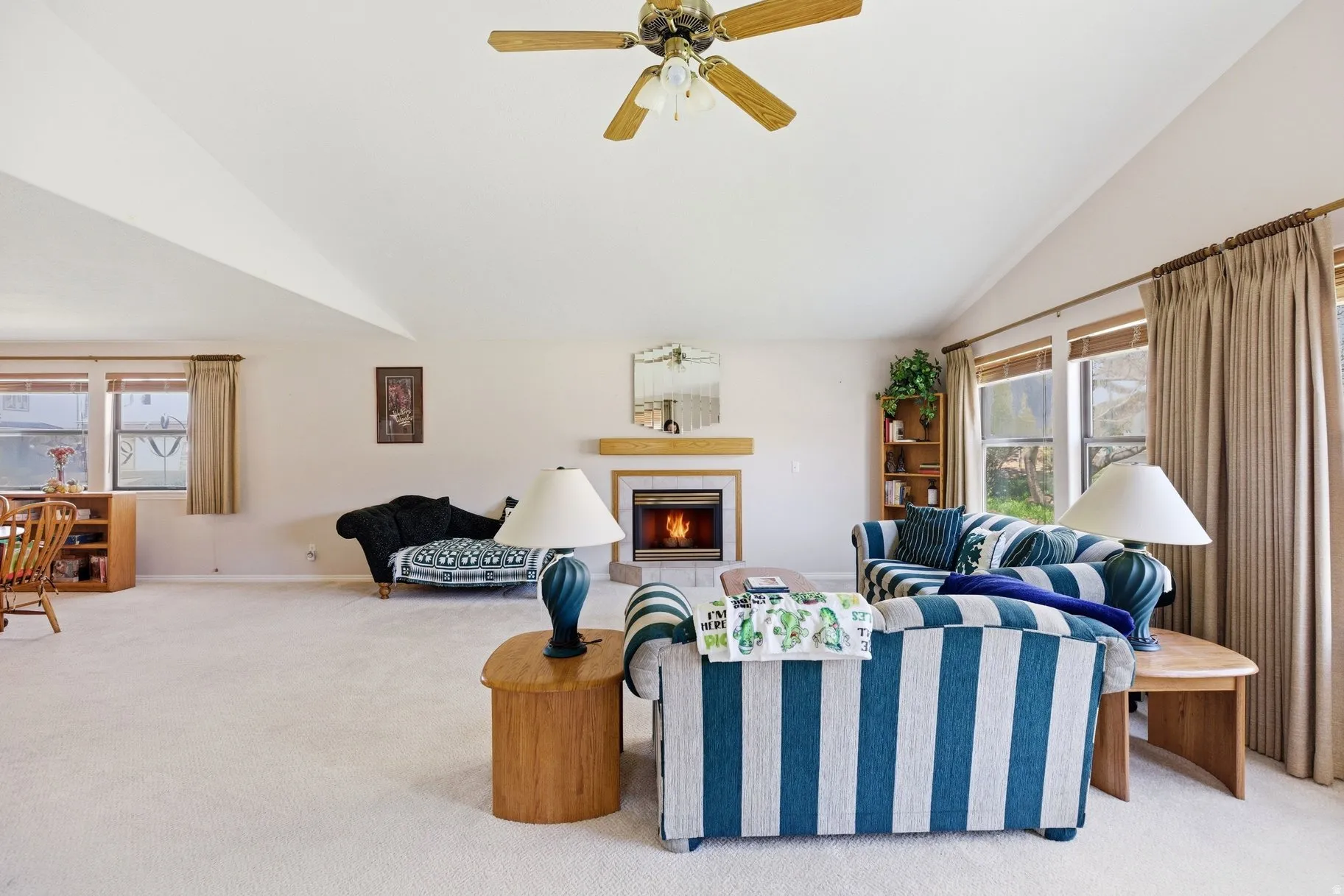 Living area featuring light carpet, a ceiling fan, vaulted ceiling, a fireplace, and healthy amount of natural light