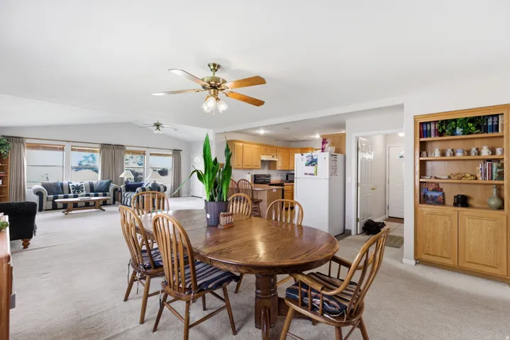 Dining area featuring light colored carpet, ceiling fan, and vaulted ceiling