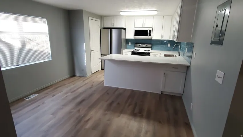 Kitchen featuring a peninsula, white cabinetry, white stove, backsplash, and electric panel