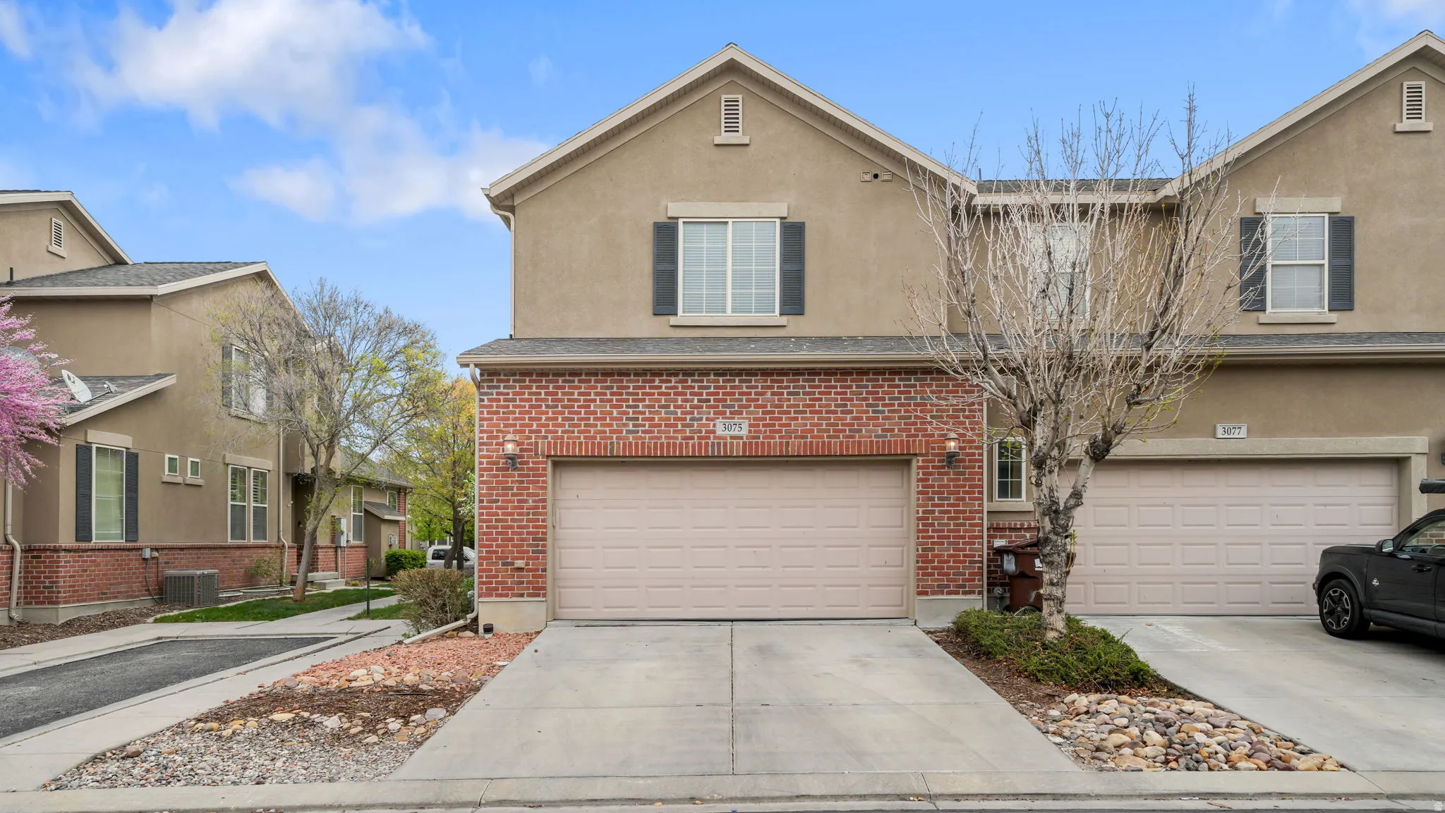 Traditional-style home with a garage, brick siding, driveway, and stucco siding