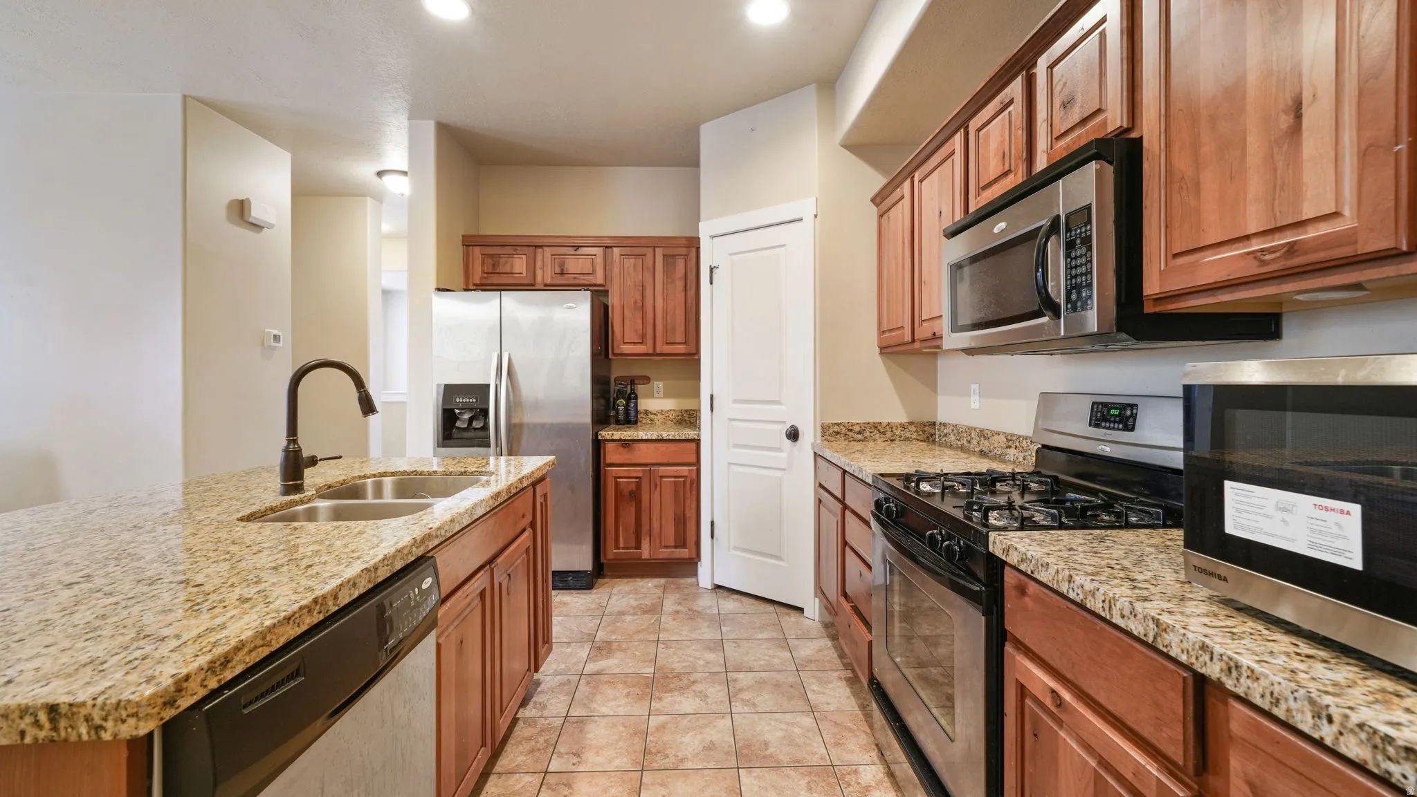 Kitchen featuring stainless steel appliances, wood finish cabinets, light stone counters, and a center island with sink