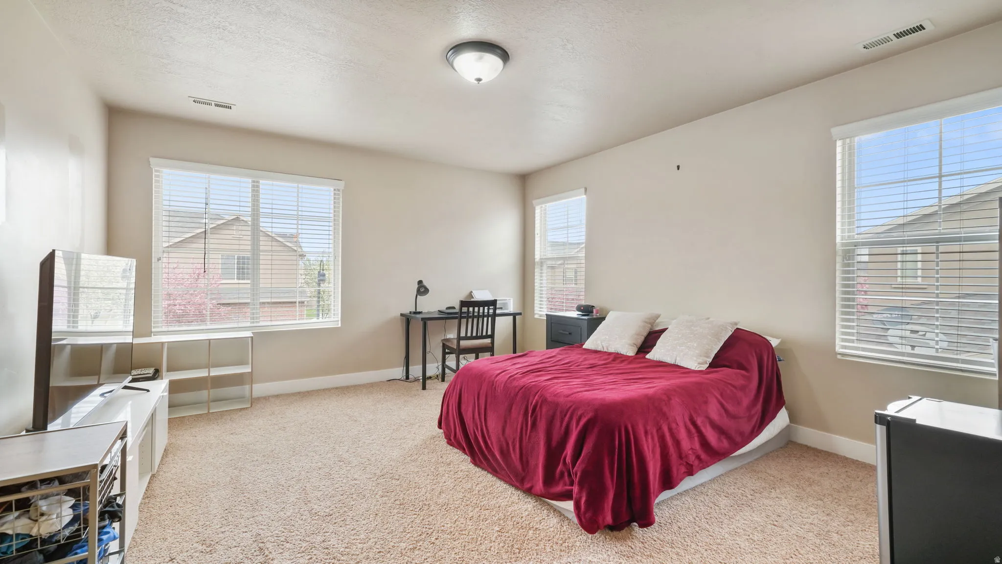 Bedroom with light colored carpet, multiple windows, and a textured ceiling