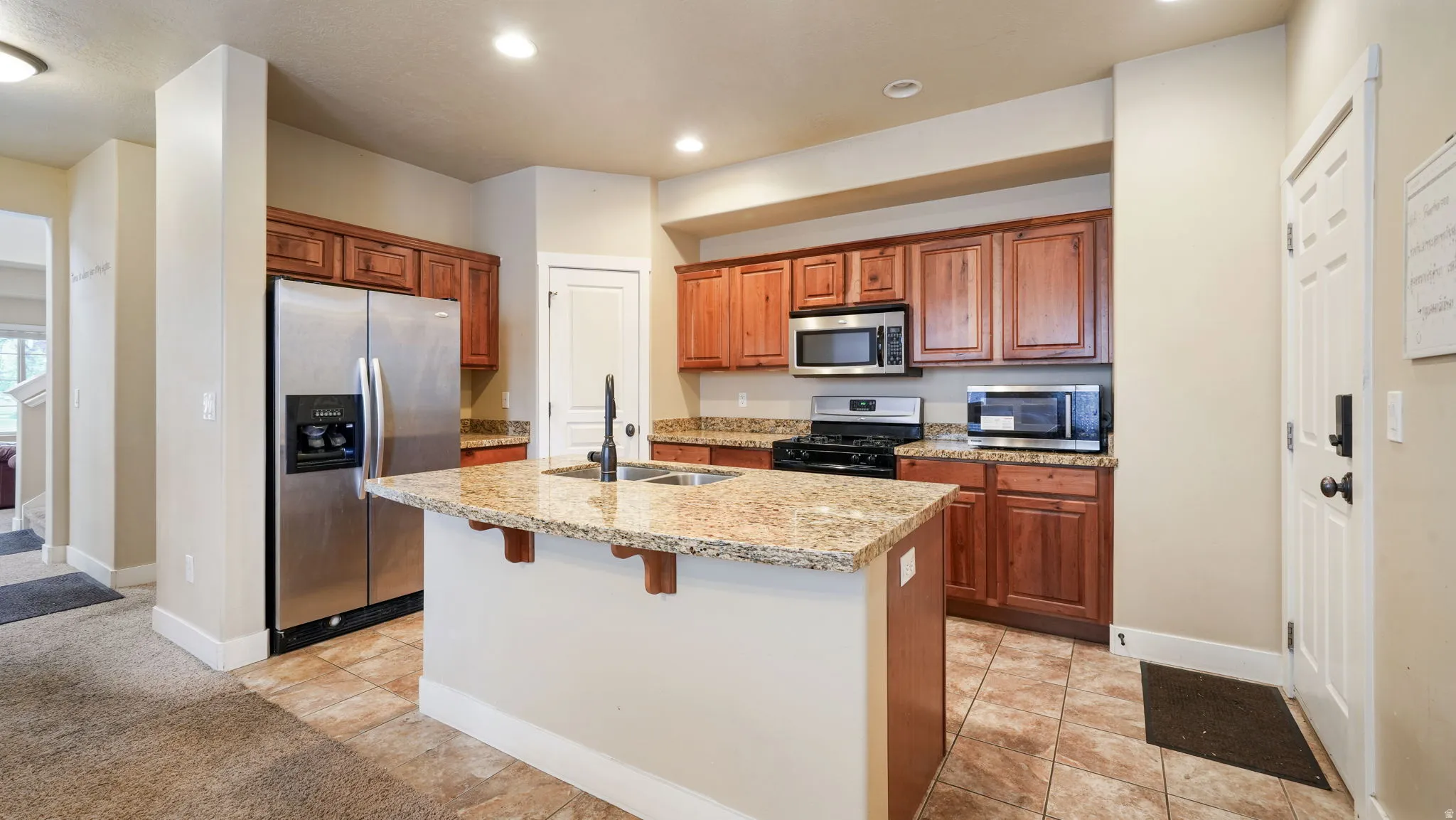 Kitchen featuring stainless steel appliances, light stone counters, a center island with sink, wood finish cabinetry, and a kitchen bar