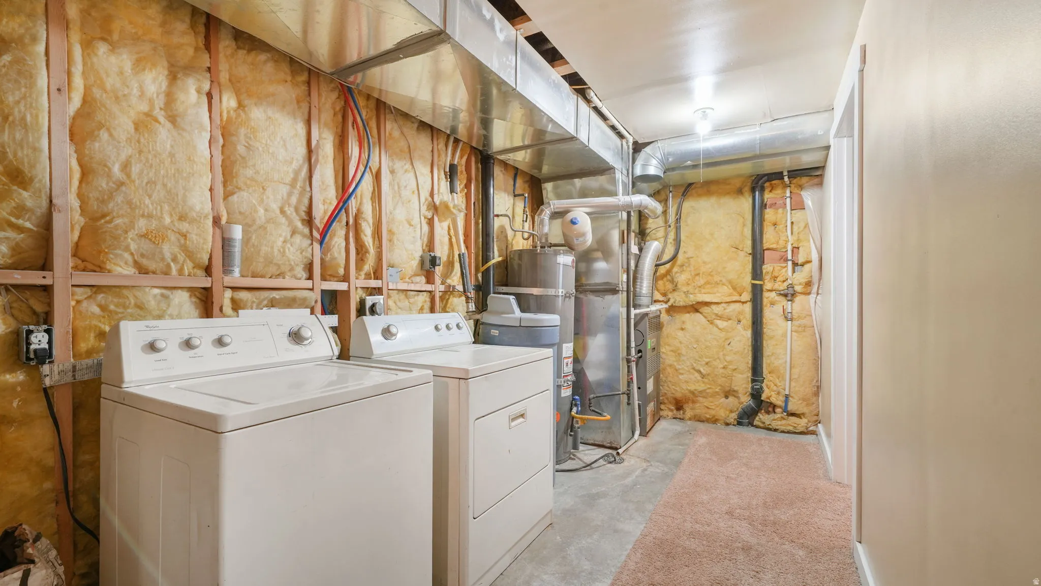 Laundry area featuring washing machine and dryer, unfinished concrete floors, and strapped water heater