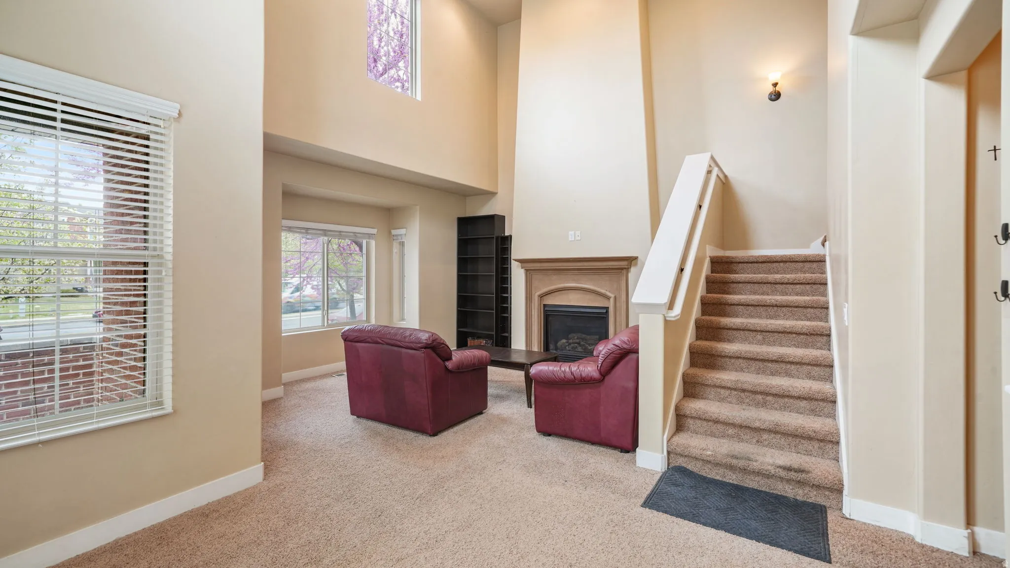 Living room featuring light colored carpet, a high ceiling, a fireplace with raised hearth, and plenty of natural light