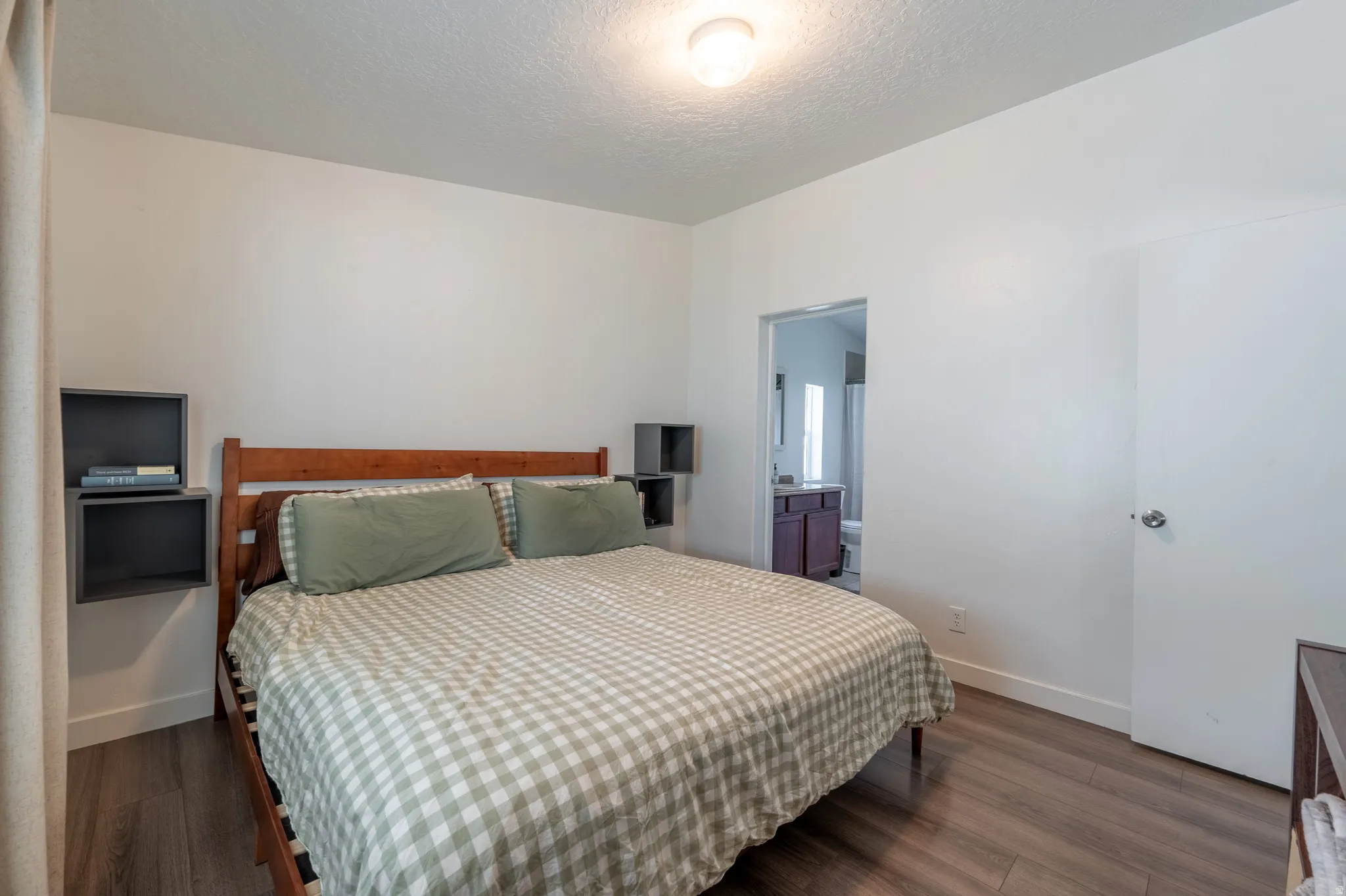 Bedroom with dark wood-style floors, a textured ceiling, and ensuite bathroom
