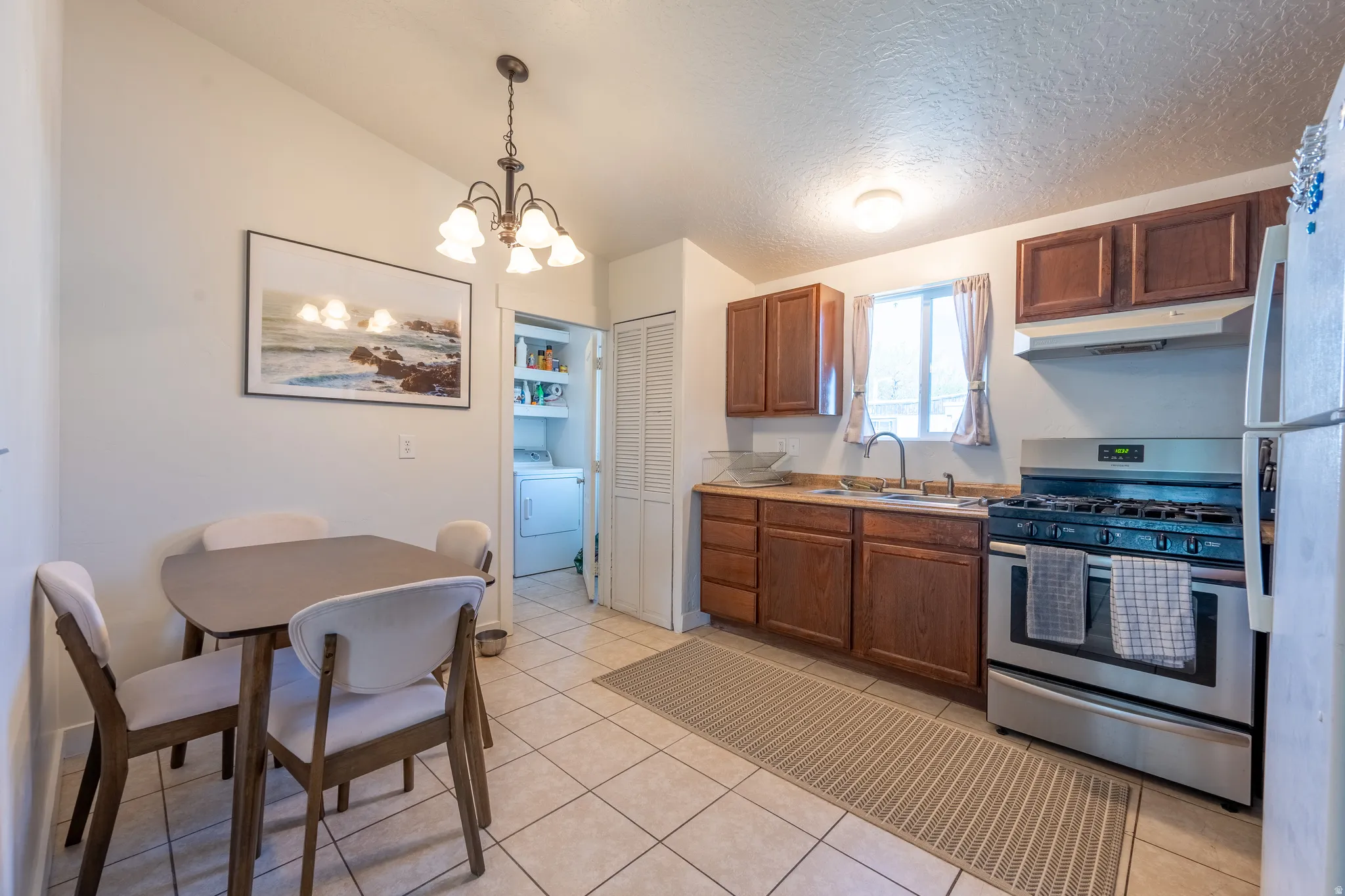 Kitchen featuring stainless steel appliances, a chandelier, light countertops, wood finish cabinetry, and washer / dryer