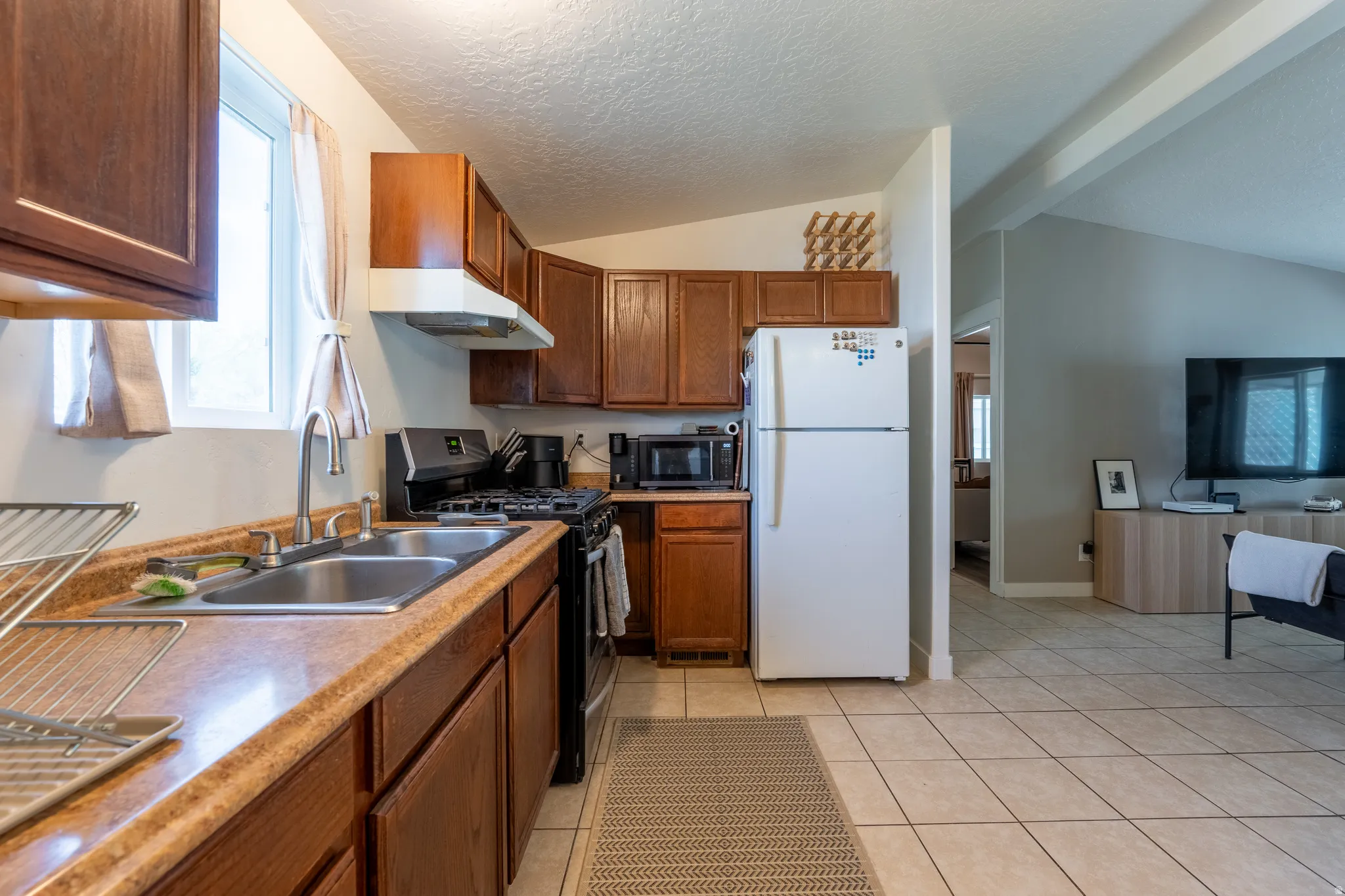 Kitchen with gas range, freestanding refrigerator, plenty of natural light, wood finish cabinetry, and beamed ceiling