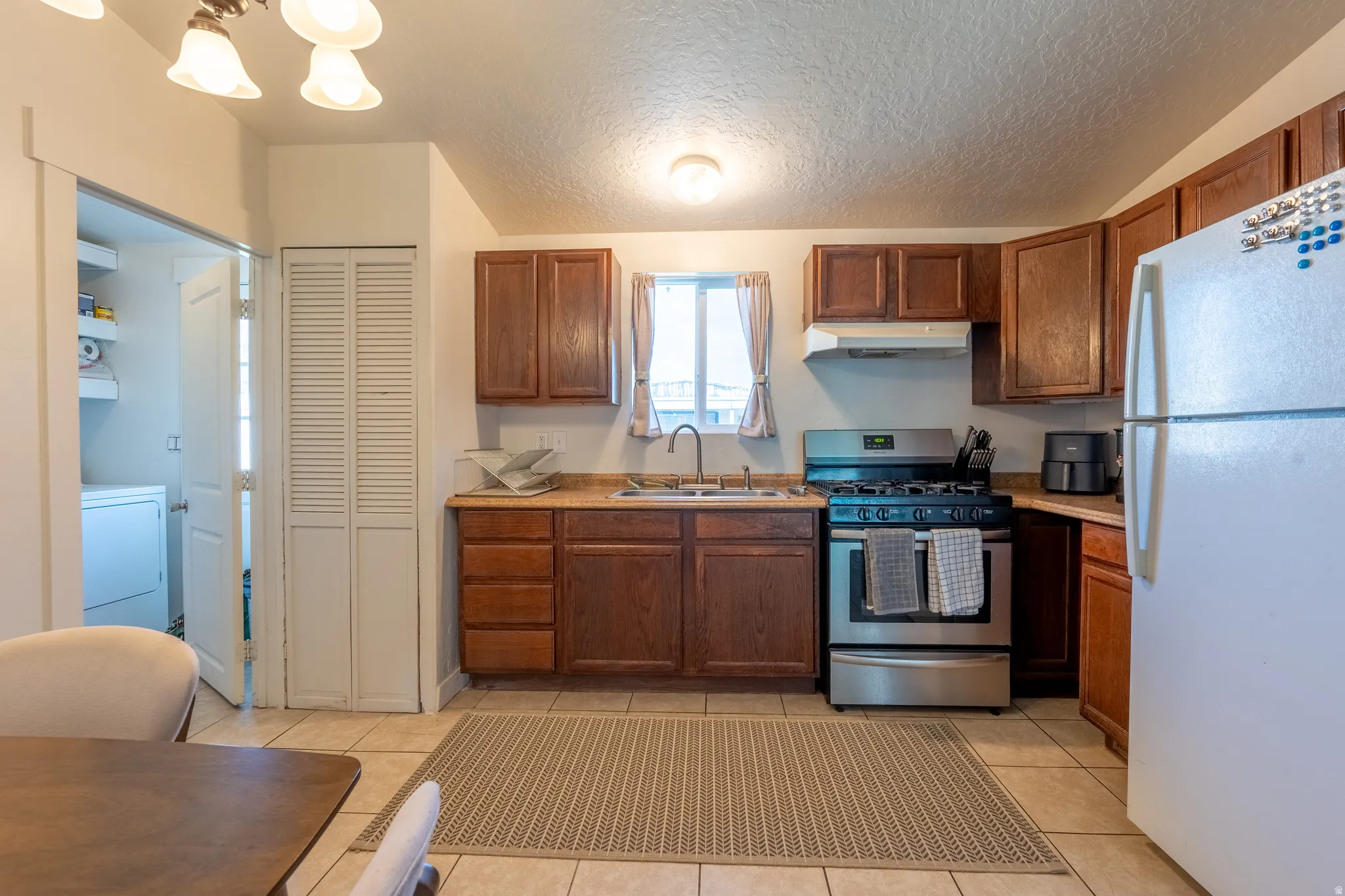 Kitchen featuring stainless steel gas range oven, freestanding refrigerator, light countertops, a textured ceiling, and washer / dryer