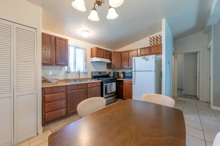 Kitchen with freestanding refrigerator, stainless steel range with gas cooktop, hanging lights, wood finish cabinets, and light countertops